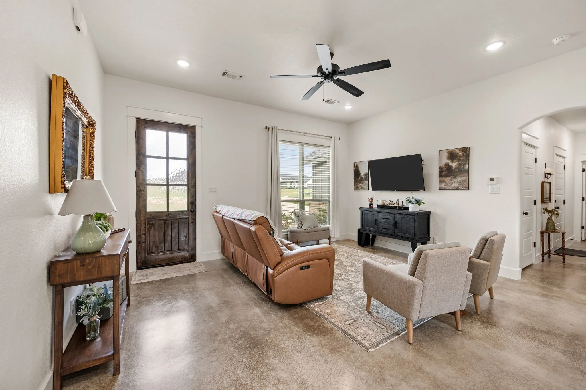 Spacious living area featuring polished concrete flooring, recessed lighting, a modern ceiling fan, and a rustic wood-finish front door with glass panels