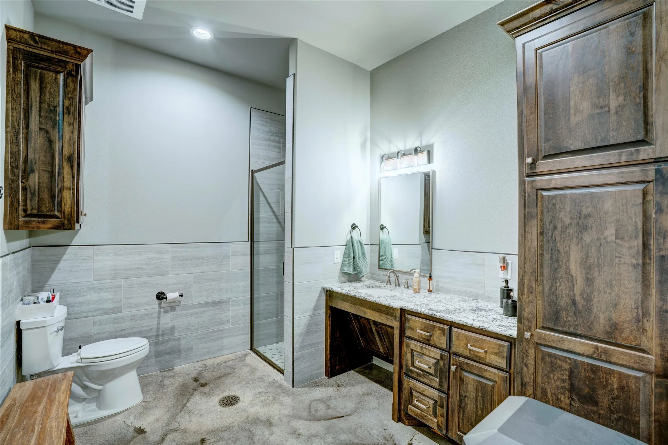 Bathroom featuring a glass-enclosed shower, wood-finish cabinetry, a white toilet, and a vanity with a white countertop and undermount sink