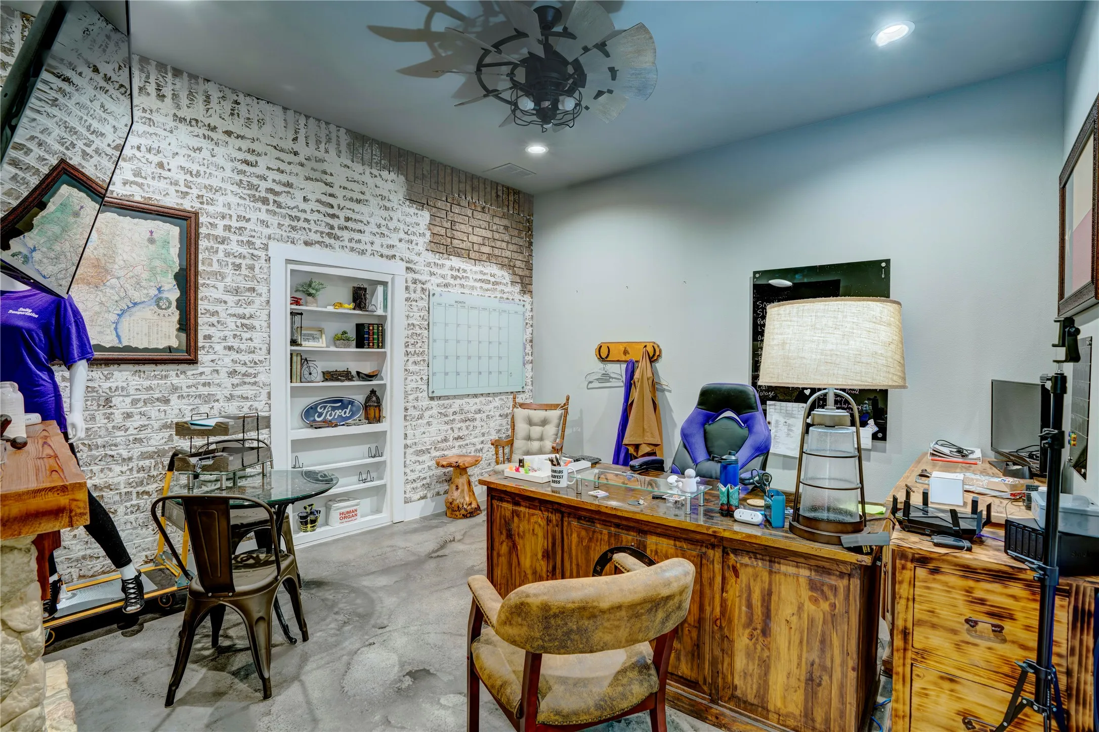 Interior space featuring a white-washed brick accent wall, built-in shelving, concrete flooring, recessed lighting, and an industrial-style ceiling fan