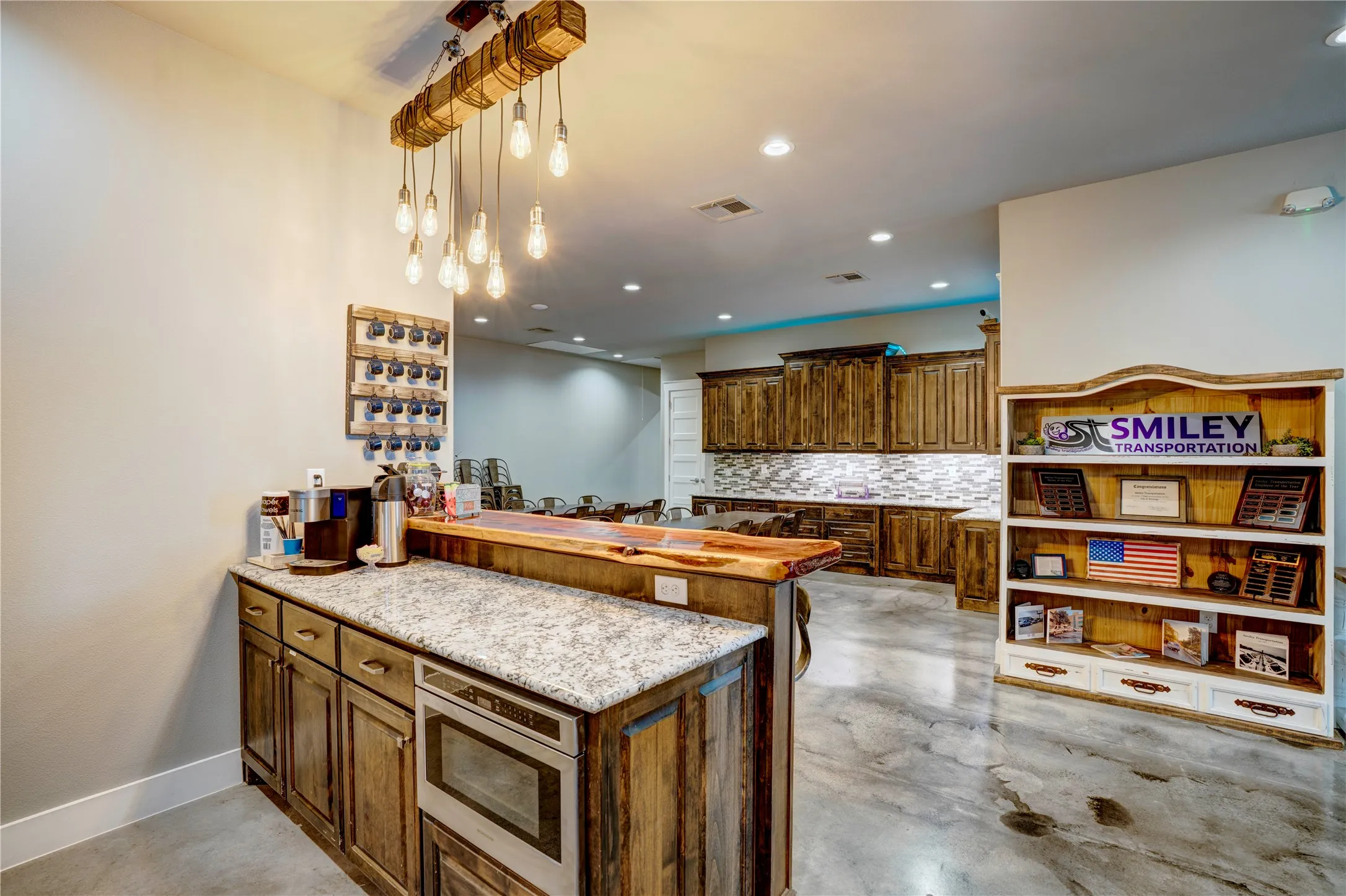 Custom wood-finish cabinetry with a built-in microwave, granite-style countertop, and suspended Edison bulb lighting