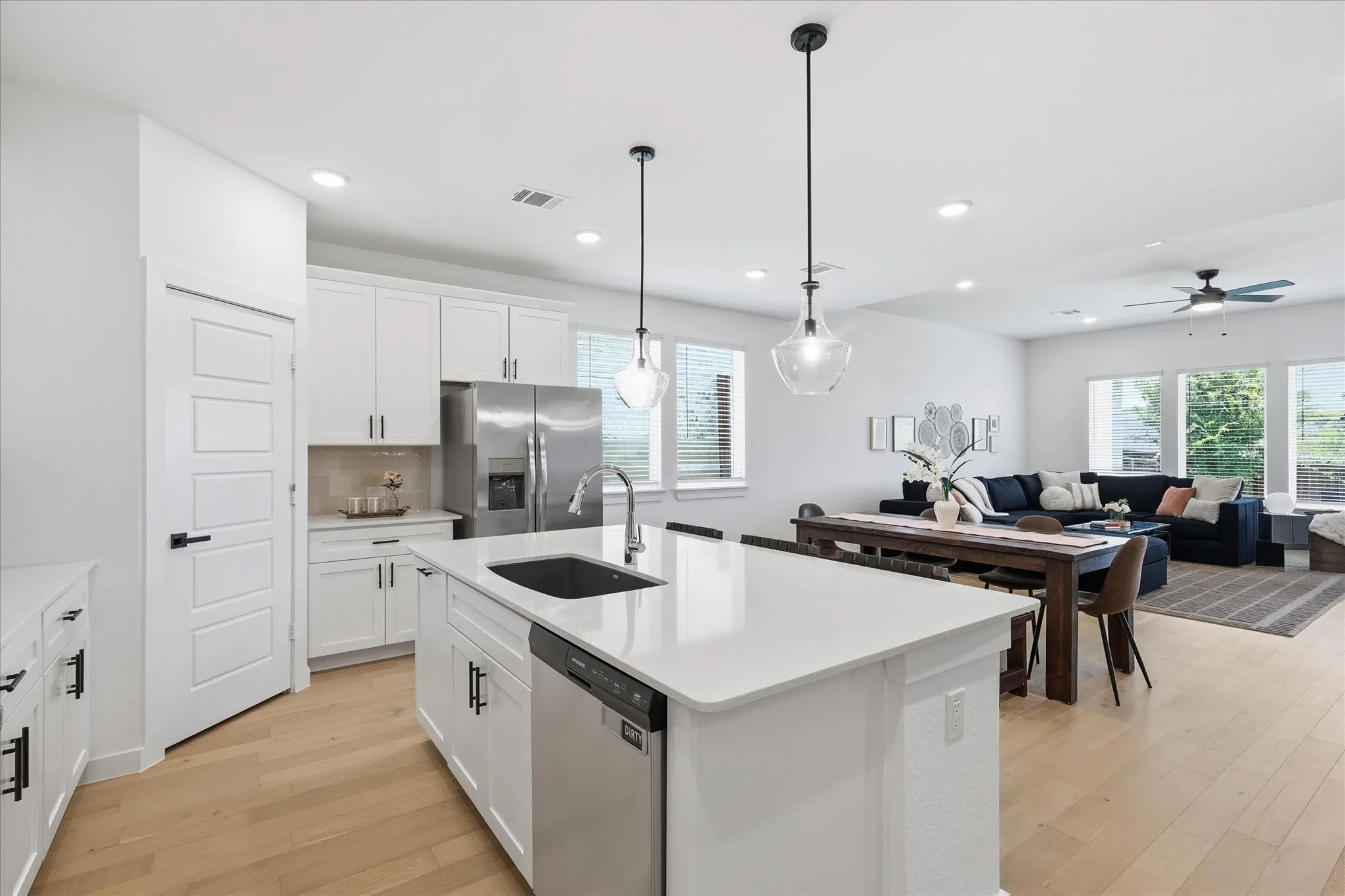 Modern kitchen featuring an expansive island with an undermount sink, white cabinetry, integrated stainless steel appliances, and wood-finish flooring
