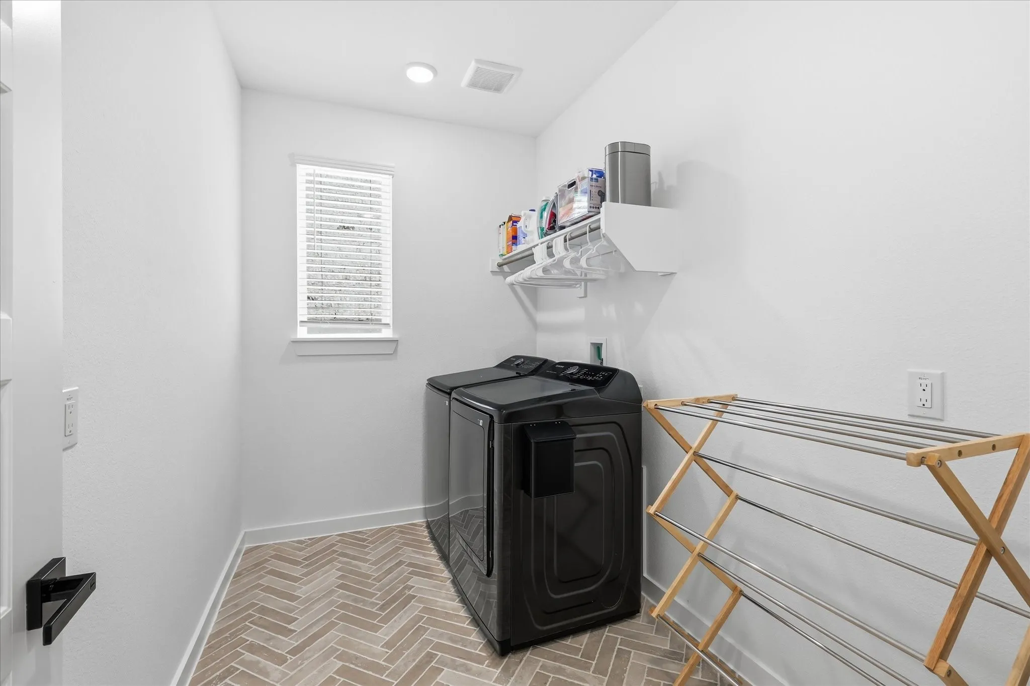 Expansive laundry room featuring herringbone tile flooring, with wall mounted shelving for additional storage space.