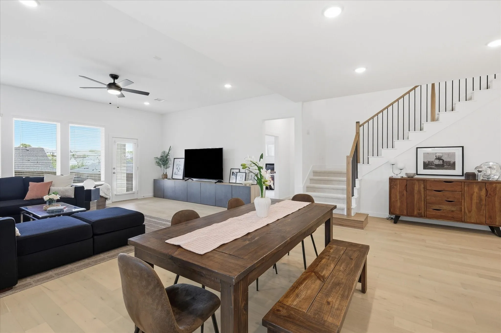 Open-concept living and dining area featuring light wood-finish flooring, recessed lighting, and a modern staircase with dark balusters