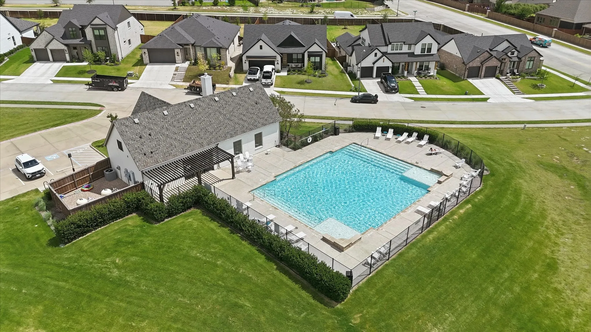 Community swimming pool with an integrated spa, surrounded by a metal fence and concrete decking