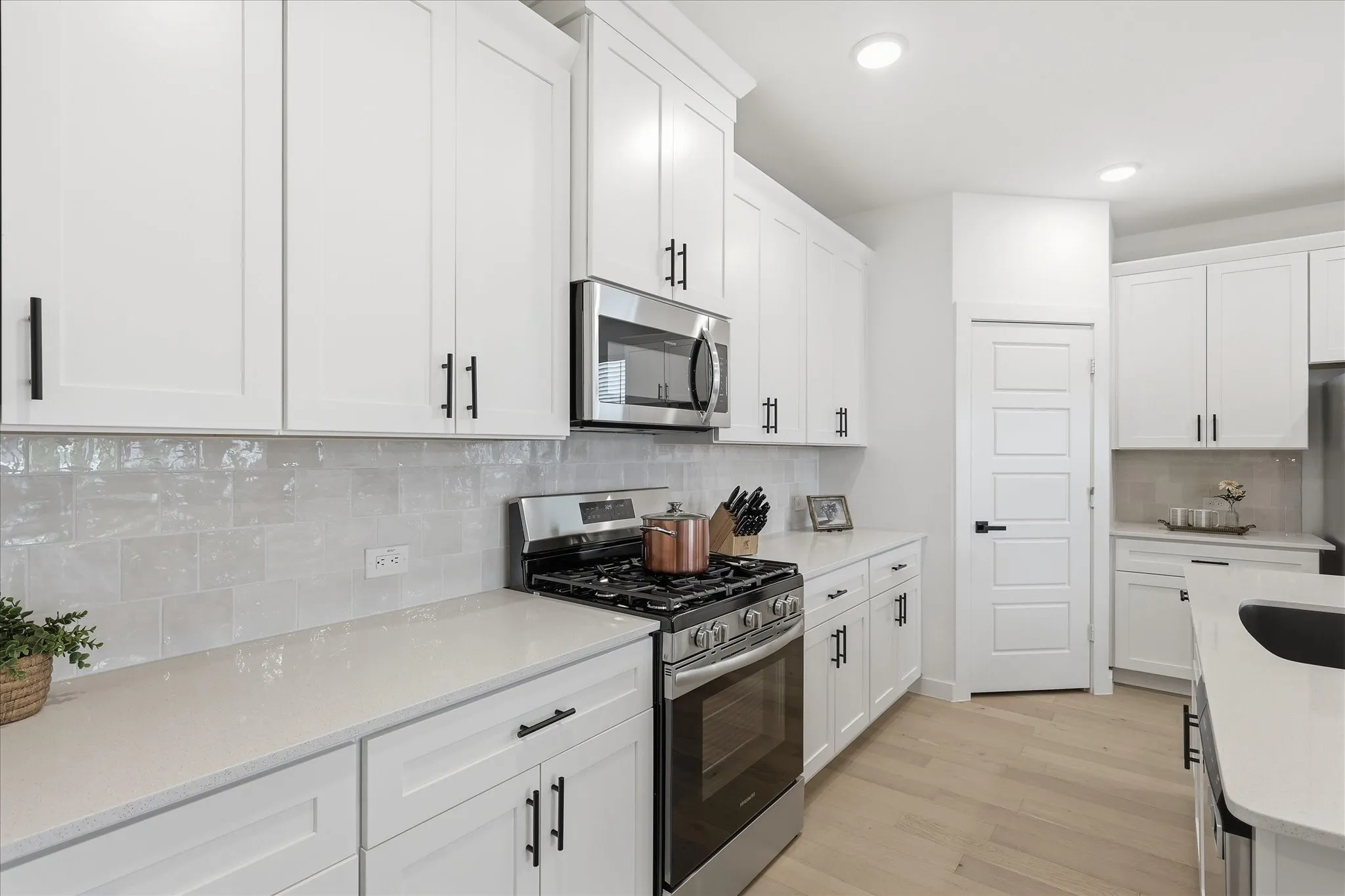 Kitchen featuring white shaker cabinetry, light-toned countertops, stainless steel appliances, a subway tile backsplash, and light wood-finish flooring