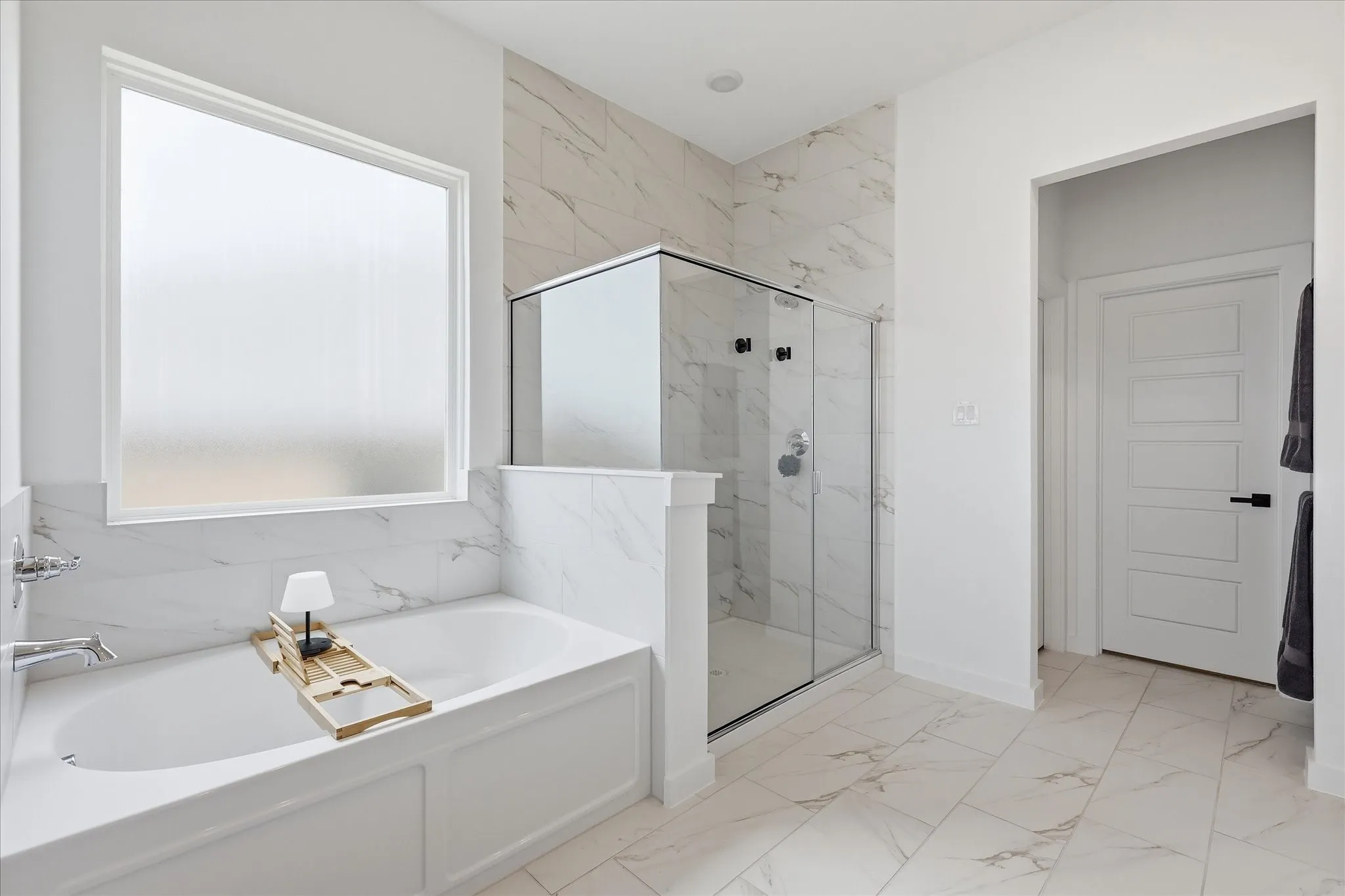 Spacious bathroom featuring a white soaking tub with chrome fixtures, a large privacy window, and a glass-enclosed shower