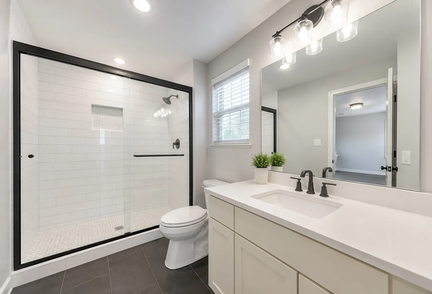 Bathroom featuring a glass-enclosed shower with subway tile surround and built-in niche, a single vanity with a white countertop and undermount sink, matte black fixtures, dark tile flooring, and a window with horizontal blinds