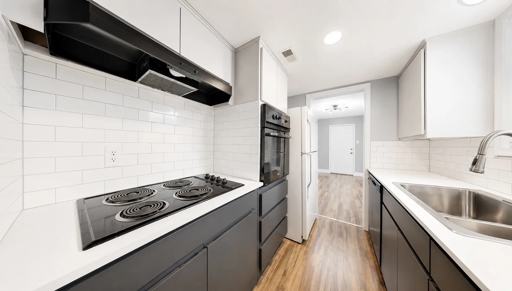 Galley kitchen featuring white subway tile backsplash, white countertops, built-in wall oven, under-cabinet lighting, and wood-finish flooring