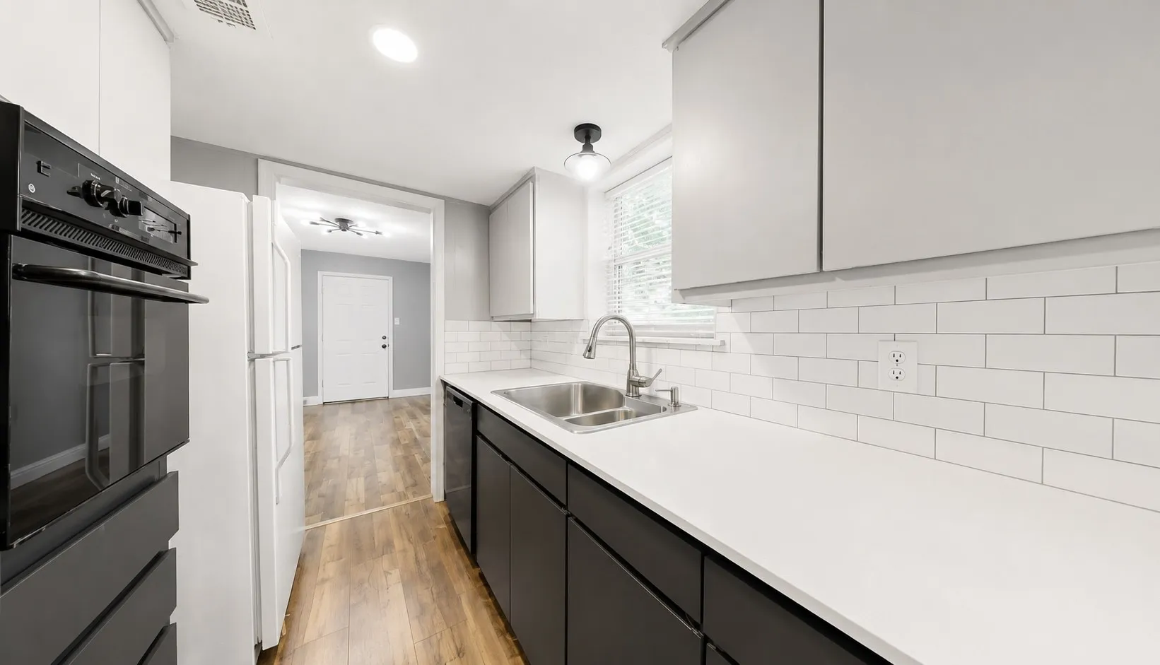 Modern kitchen featuring dual-toned cabinetry, white subway tile backsplash, and light-toned countertops