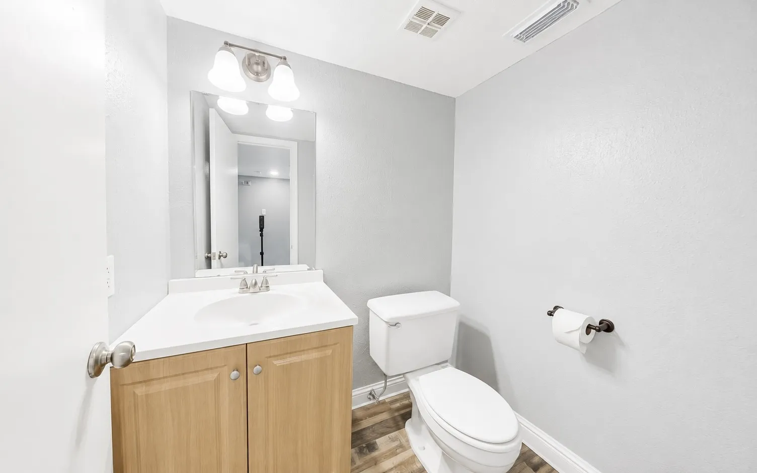 Powder room featuring a single vanity with a white countertop, wood-finish cabinetry, brushed nickel faucet, and wood-look flooring