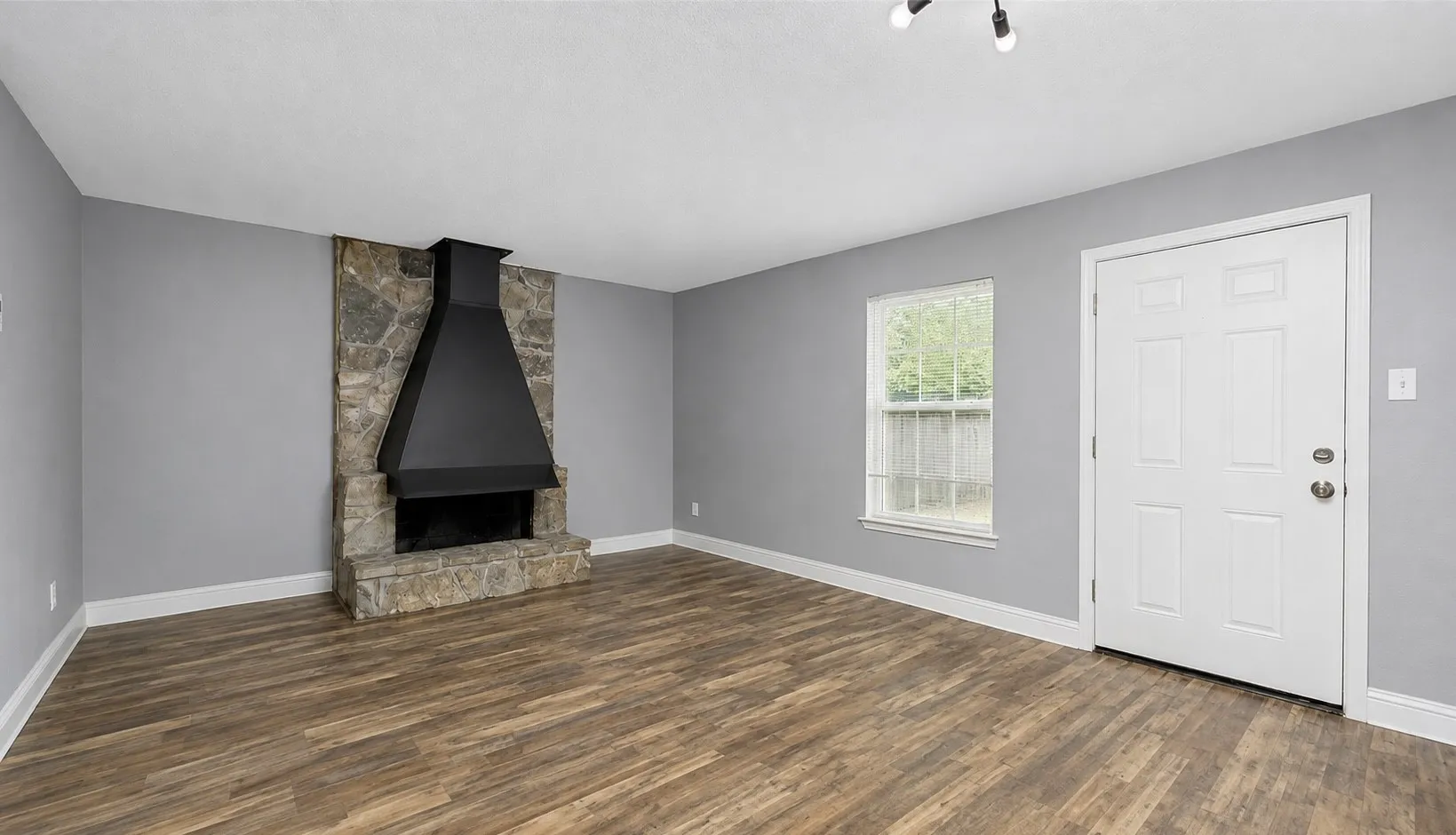 Stone fireplace with a black metal hood, wood-finish flooring, light gray walls, and white trim