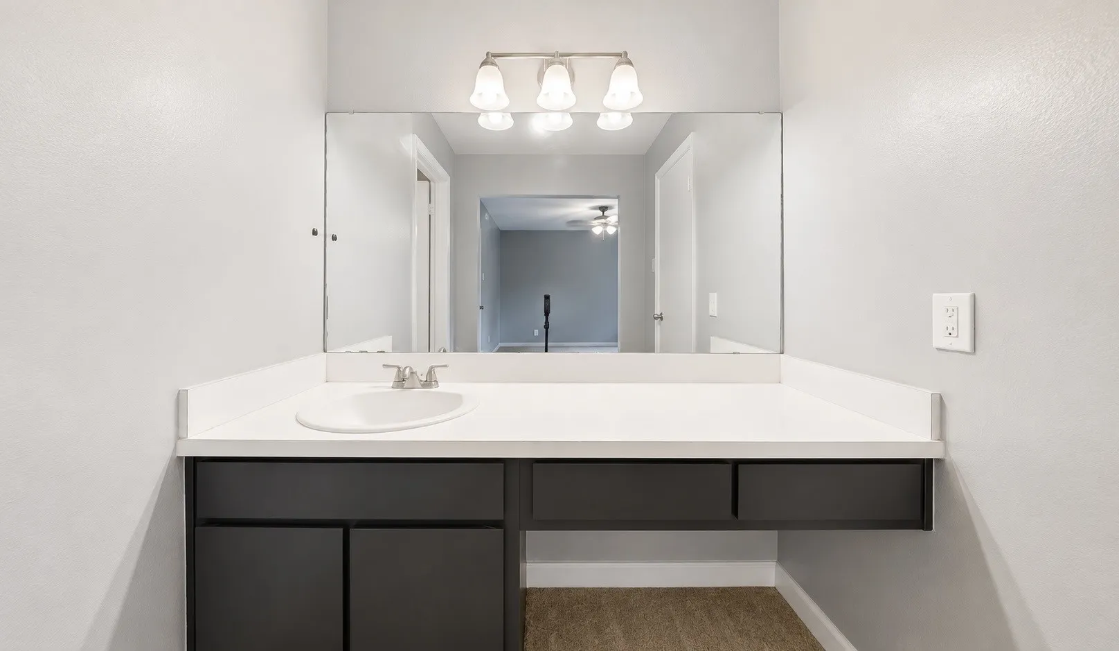 Contemporary vanity featuring a white countertop with integrated sink, dark cabinetry, and a large wall-mounted mirror