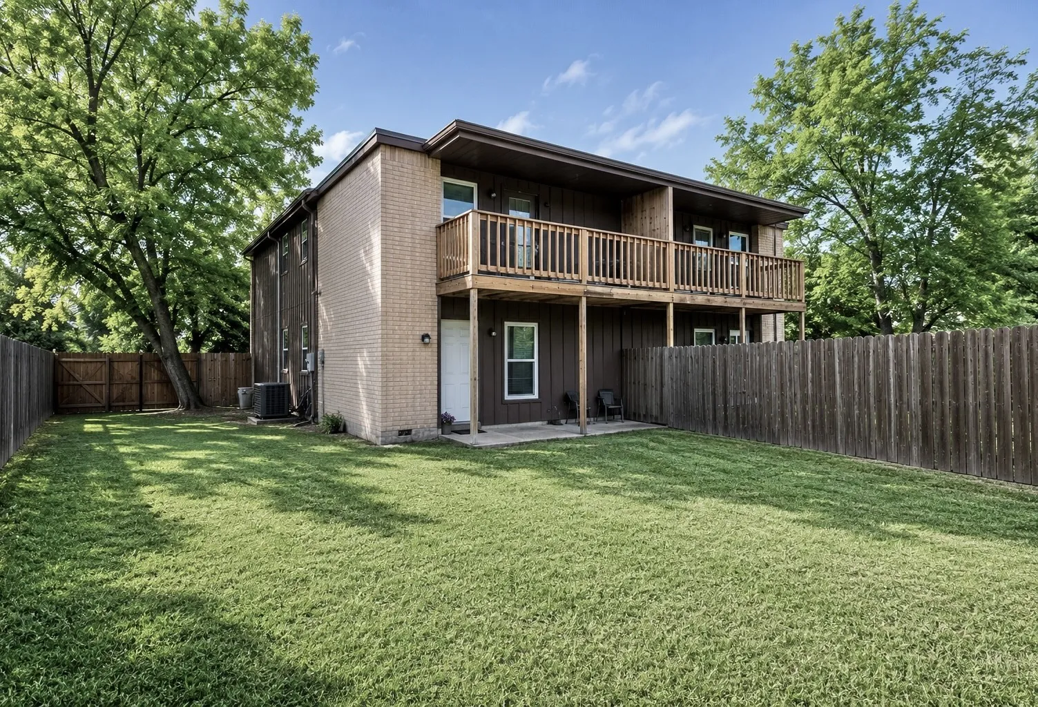 Rear exterior featuring a full-width upper-level wood deck, a lower-level concrete patio, and a privacy fence