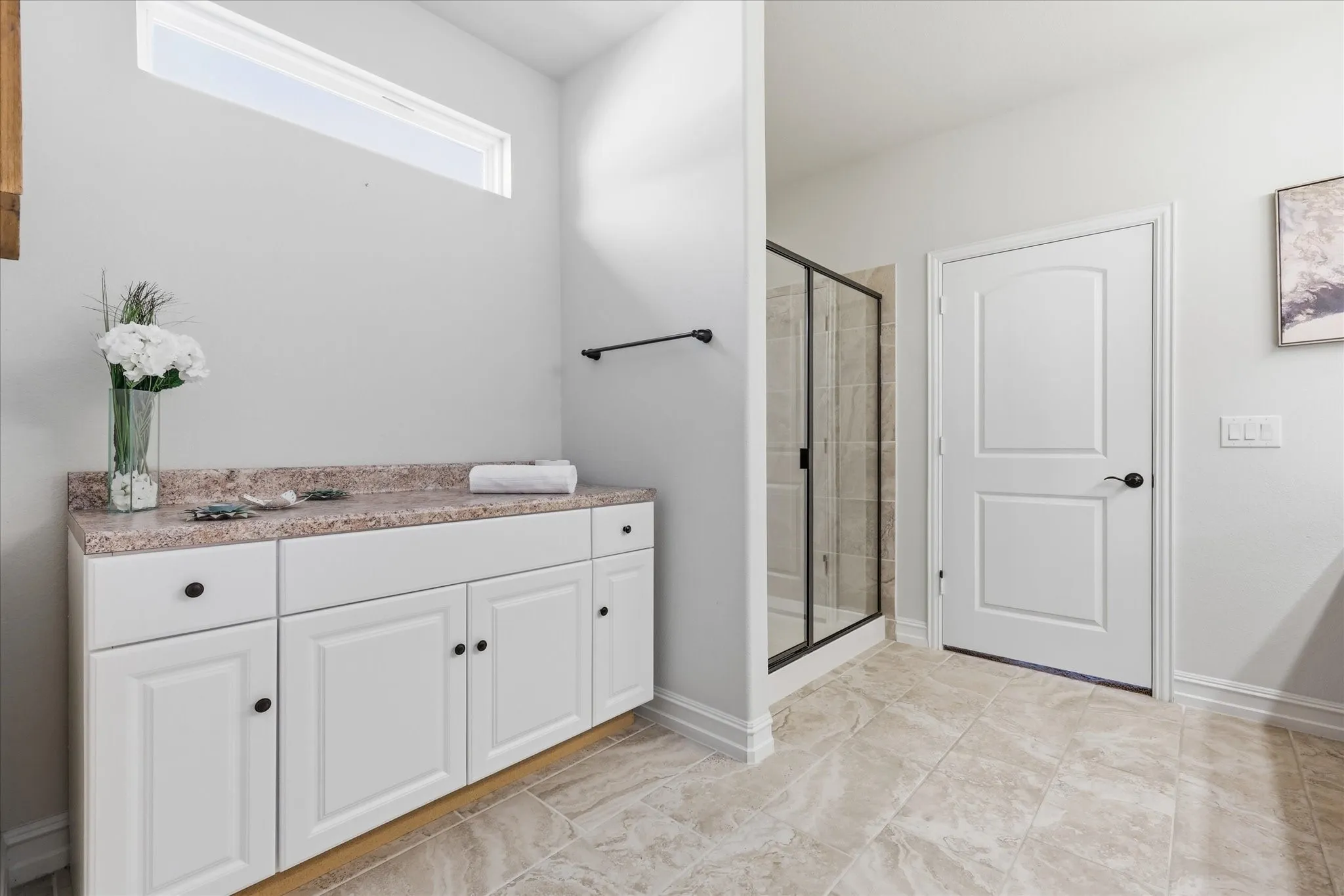 Spacious interior featuring a tiled floor, white base cabinetry with dark hardware, a walk-in shower with a glass enclosure, and a high transom window