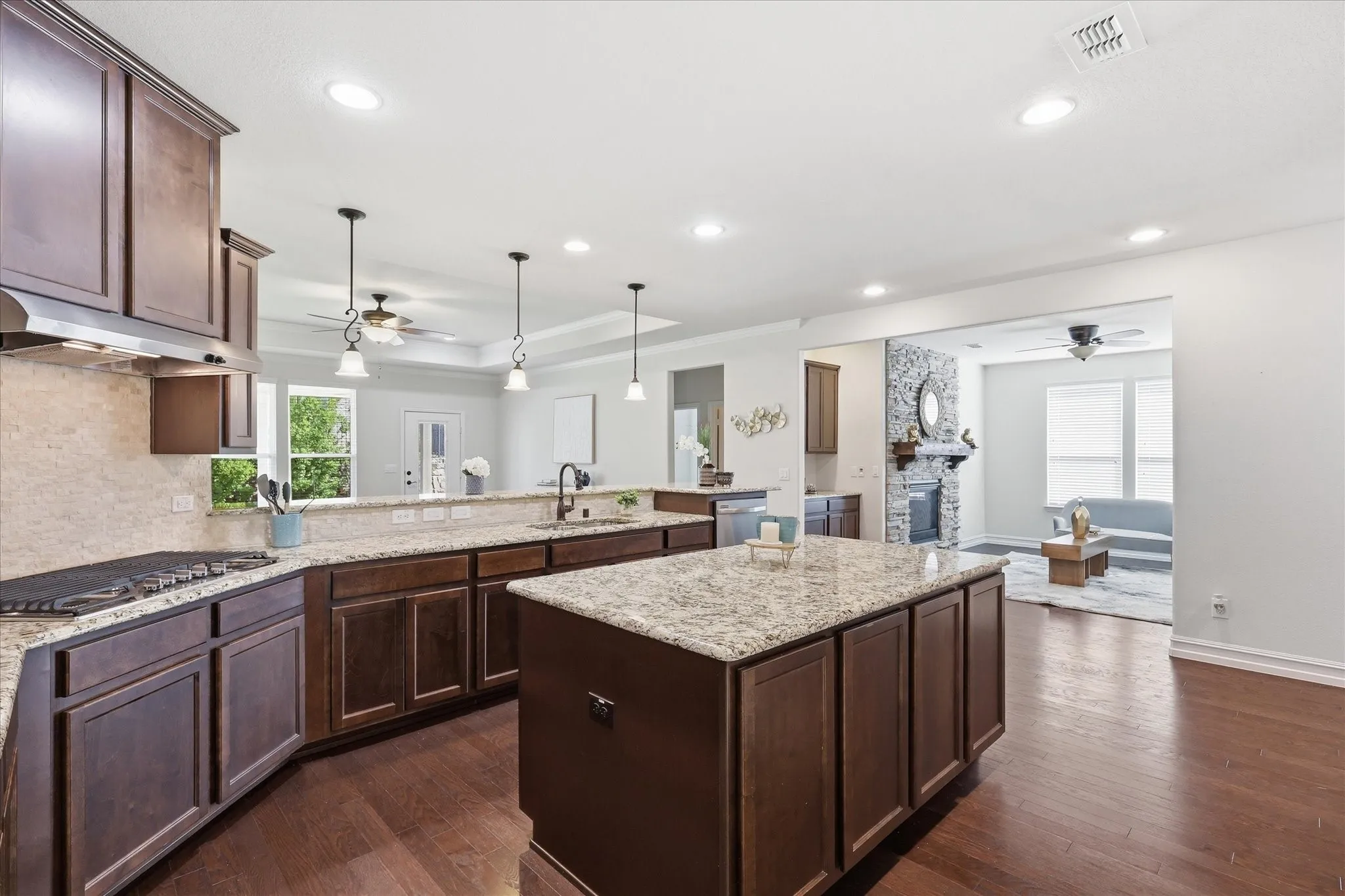 Spacious kitchen featuring an island with granite countertops, dark wood-finish cabinetry, built-in gas cook top with stainless steel hood, and a tile backsplash