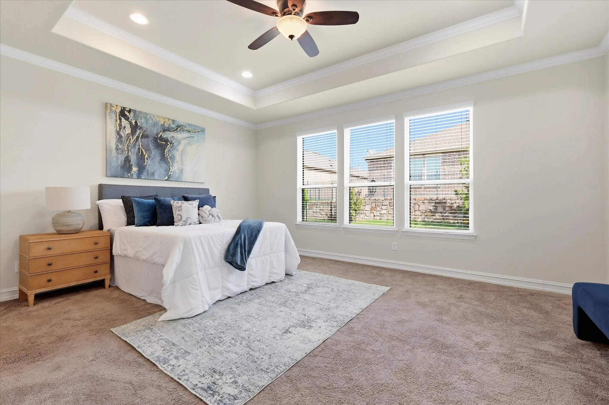 Spacious Primary bedroom featuring a tray ceiling with recessed lighting and a ceiling fan, three large windows with blinds, plush carpet flooring, and white baseboards