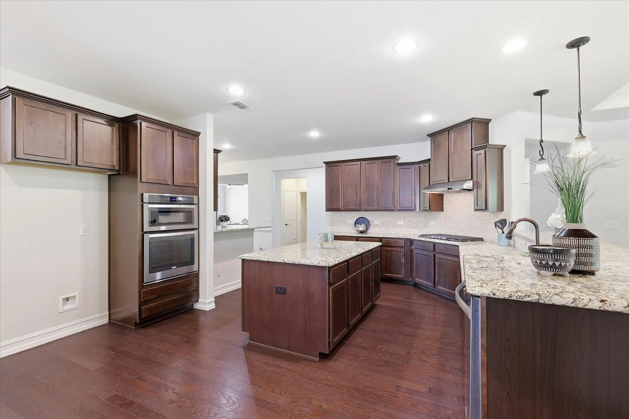 Spacious kitchen featuring dark wood cabinetry, granite countertops, a central island, built-in oven and microwave, and wood-finish flooring
