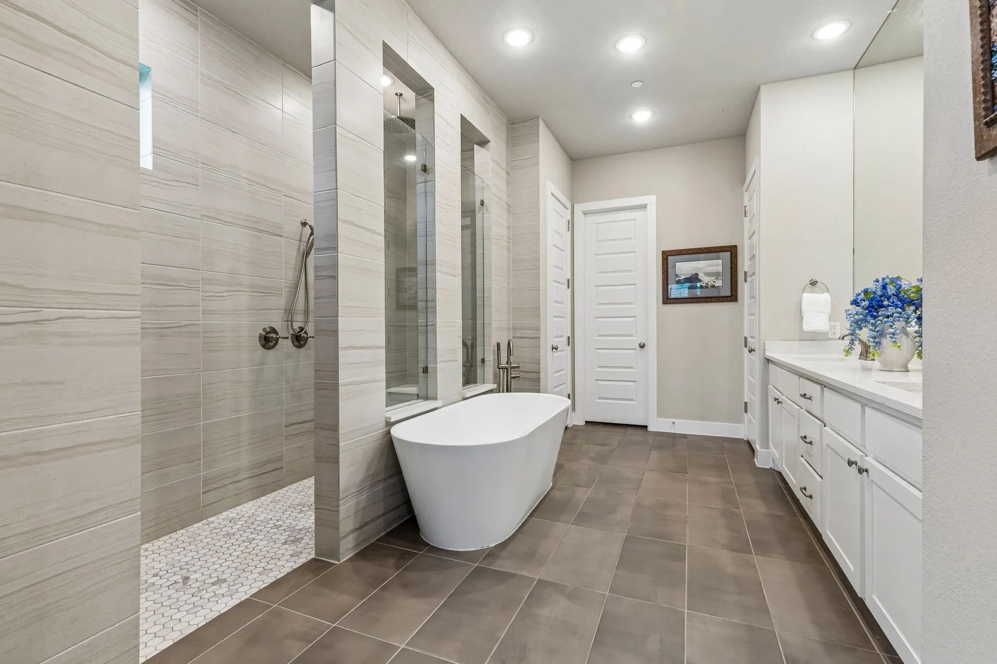 Primary suite spa bath with soaking tub, extended vanity with double sinks, oversized walk-in shower with rain head and dual benches, and direct access to the laundry room through the custom walk-in closet.