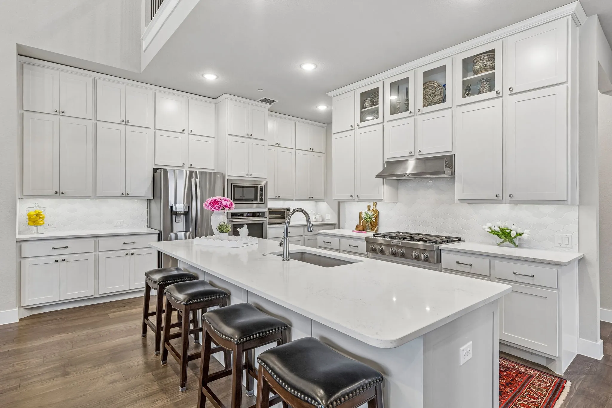 The gourmet kitchen features a large center island with seating, KitchenAid six-burner range, quartz counters, soft-close cabinetry, built-in oven and microwave, and walk-in pantry.
