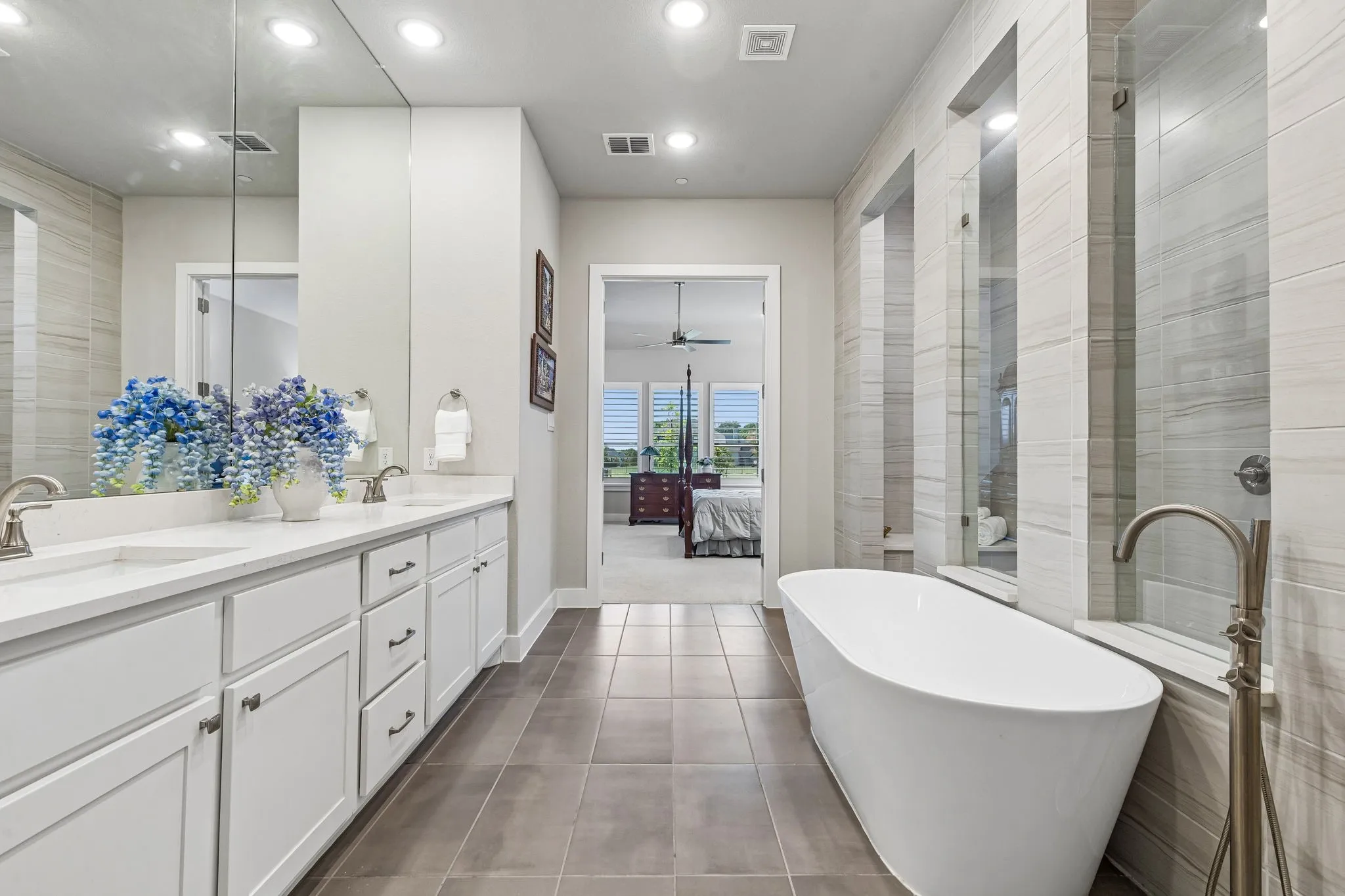 Primary suite spa bath with soaking tub, extended vanity with double sinks, oversized walk-in shower with rain head and dual benches, and direct access to the laundry room through the custom walk-in closet.