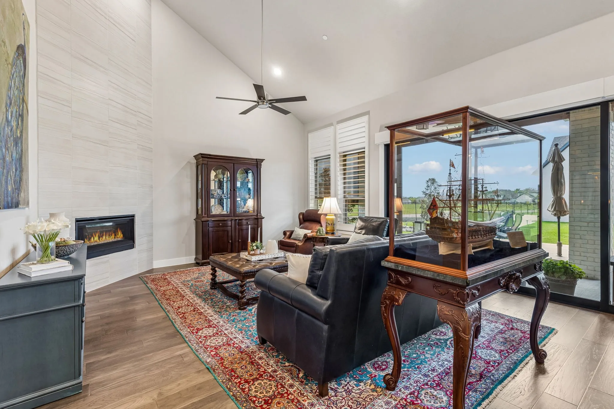 The grand living room features vaulted ceilings, a dramatic floor-to-ceiling corner fireplace, and a wall of windows overlooking the beautifully landscaped backyard.