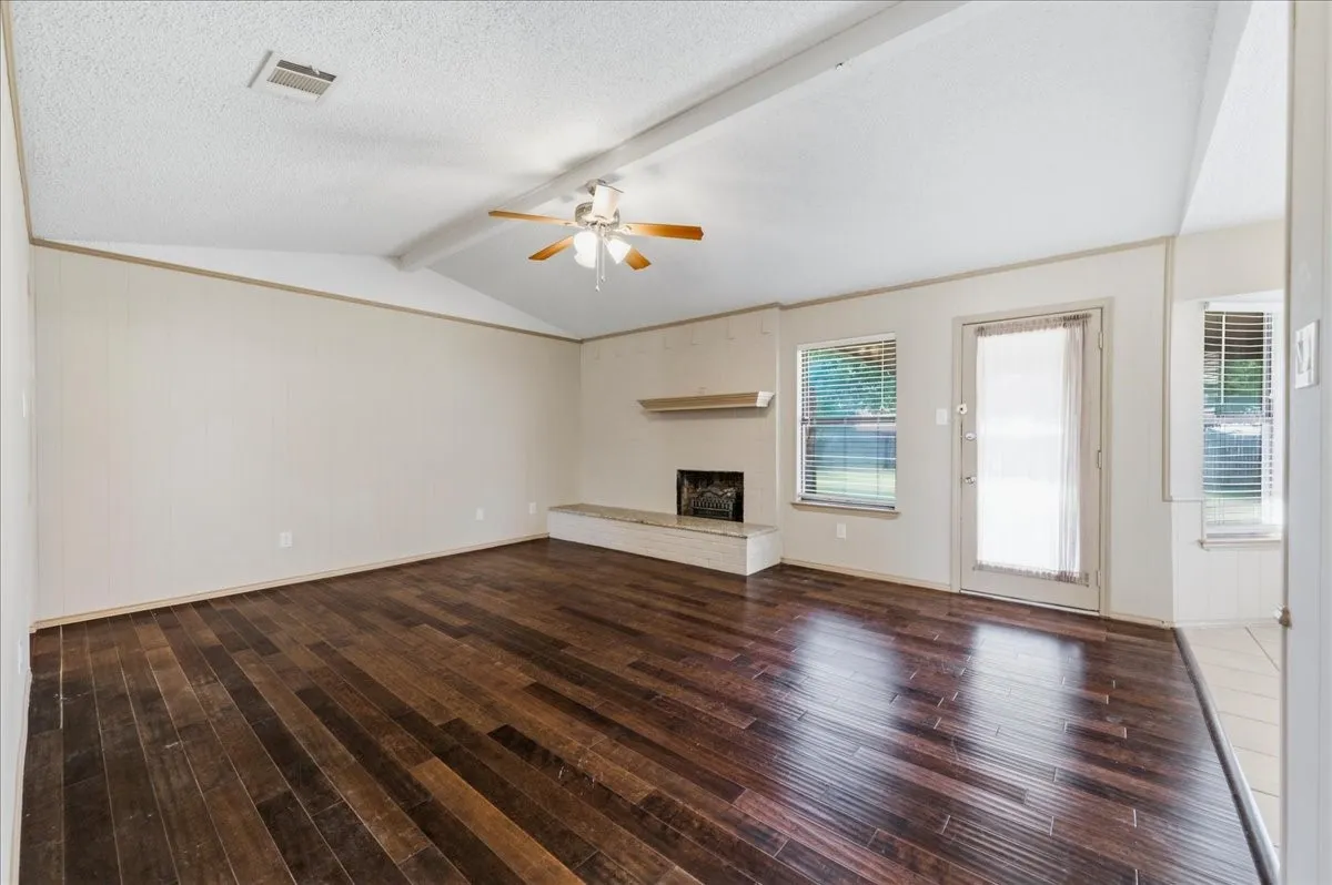 Spacious living area featuring wood-finish flooring, a vaulted ceiling, and a ceiling fan
