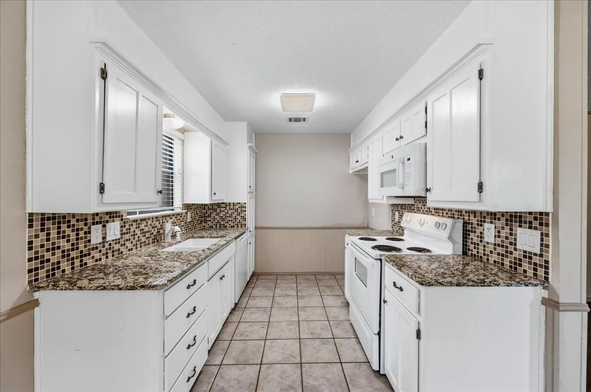Galley kitchen featuring white cabinetry, mosaic tile backsplash, patterned countertops, tile flooring, and white appliances