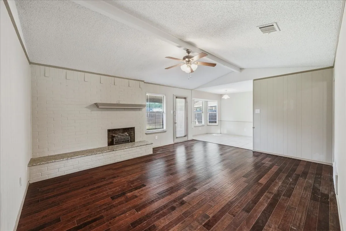 Spacious living area featuring wood-finish flooring, a painted brick fireplace with a hearth, a vaulted ceiling, and a ceiling fan