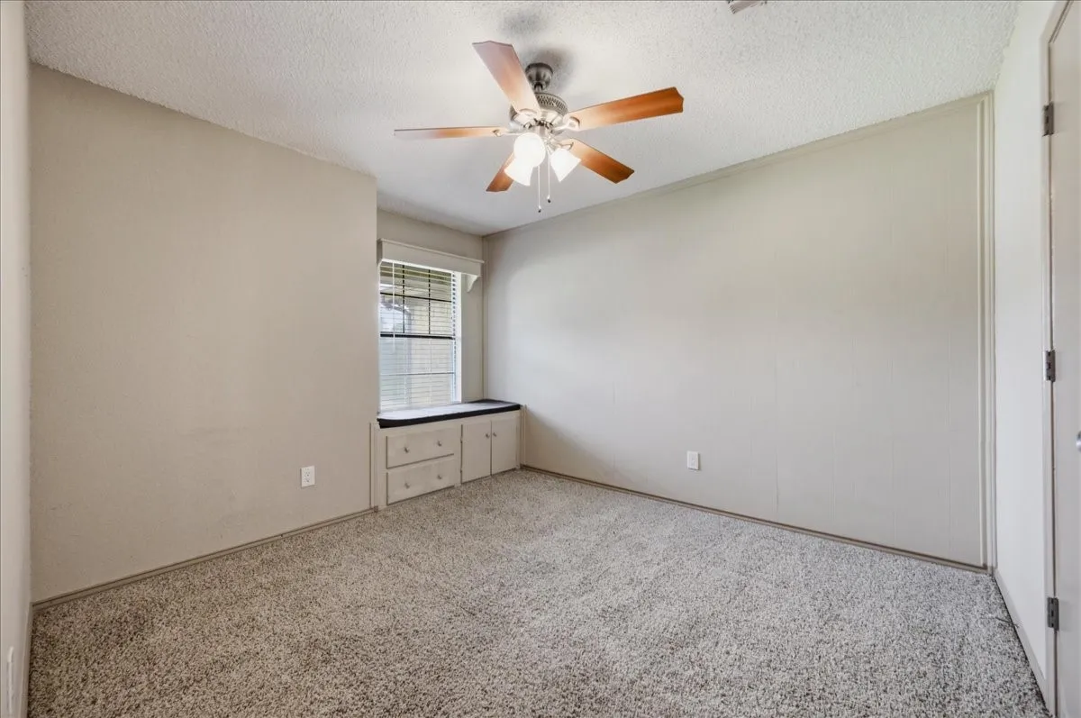 Carpeted room featuring a window with built-in cabinetry, a ceiling fan, and neutral wall tones