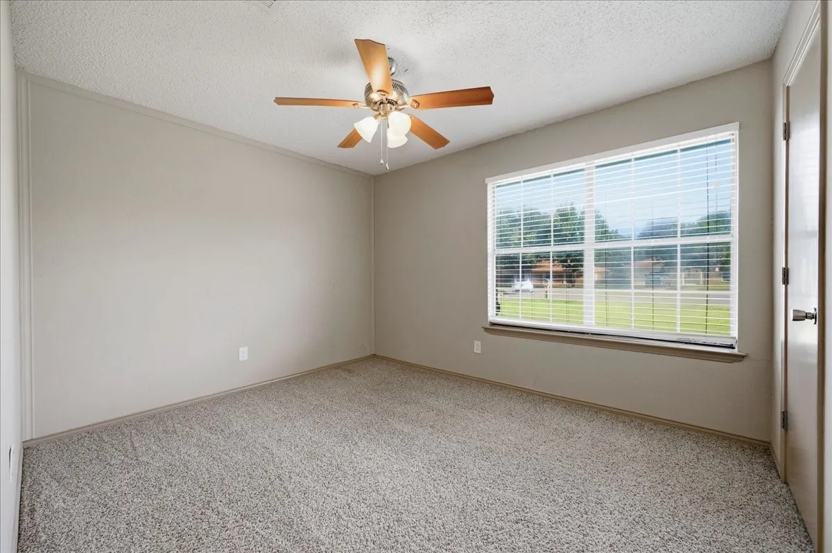 Carpeted room with a ceiling fan featuring wood-finish blades and integrated lighting