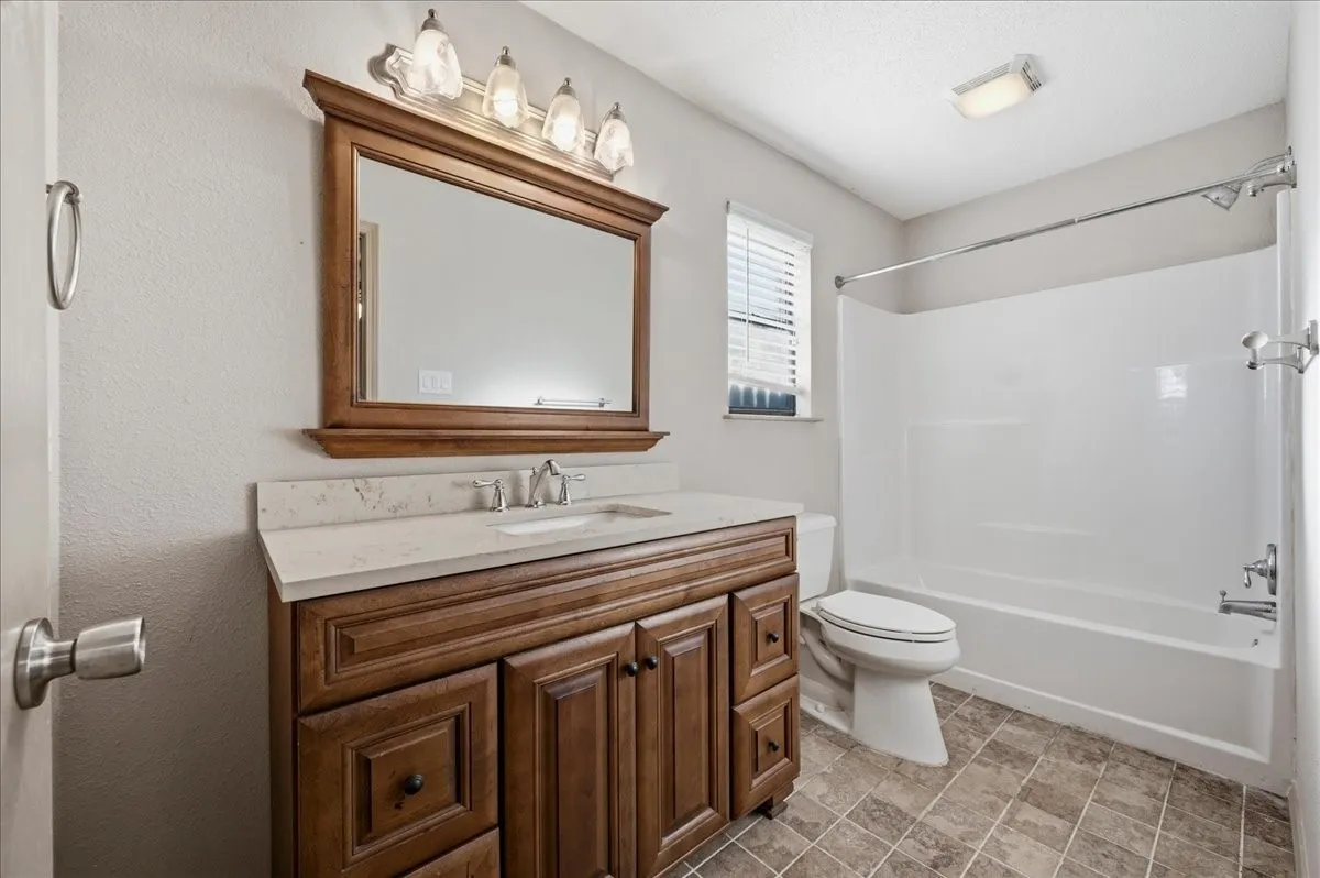 Bathroom featuring a wood-finish vanity with a light-toned countertop, an integrated sink, and a framed mirror with overhead lighting