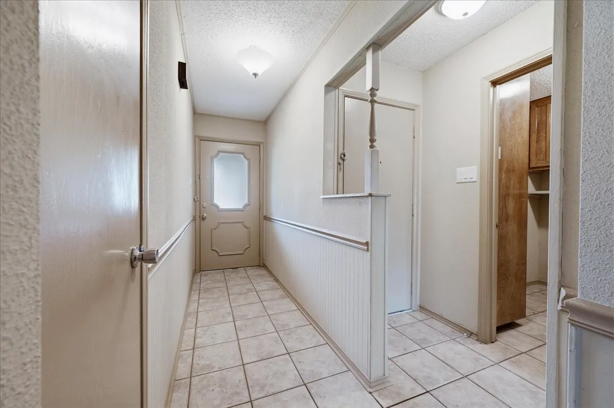 Entryway featuring light-toned square tile flooring, beadboard wainscoting, and a front door with frosted glass detailing
