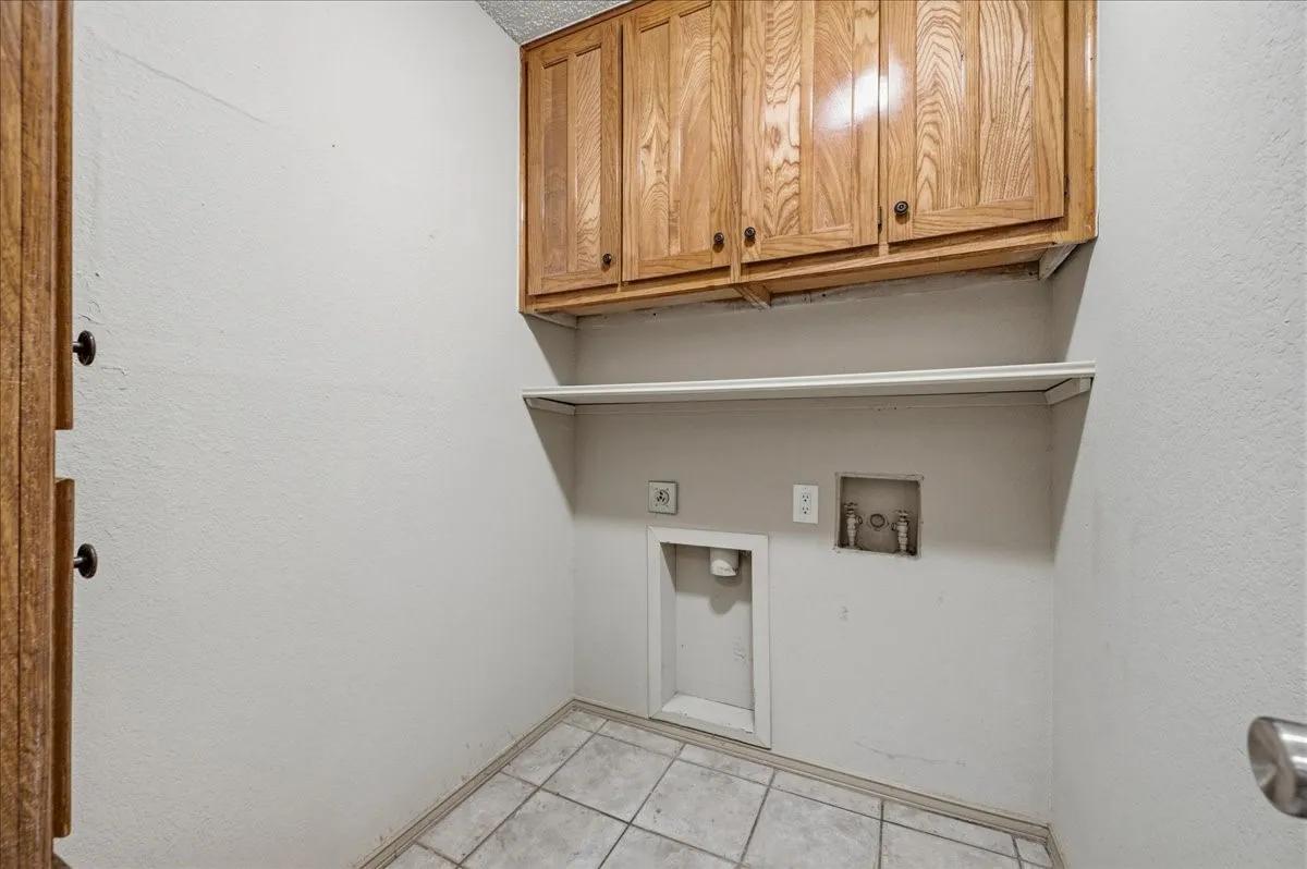 Laundry area featuring wood-finish cabinetry, a utility shelf, and tile flooring