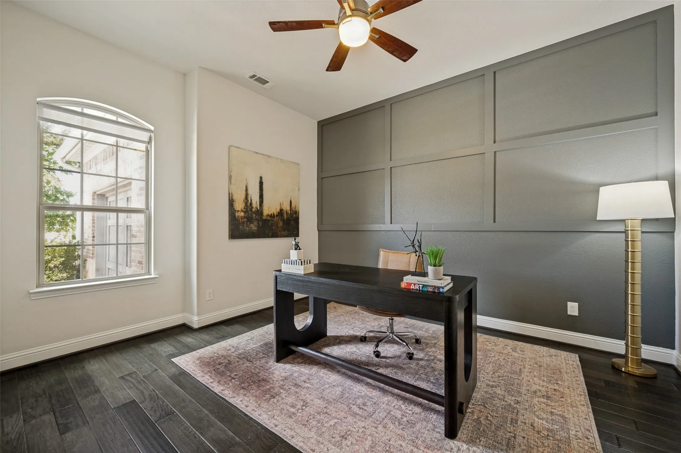 Private home office with designer accent wall, abundant natural light, and wood flooring.