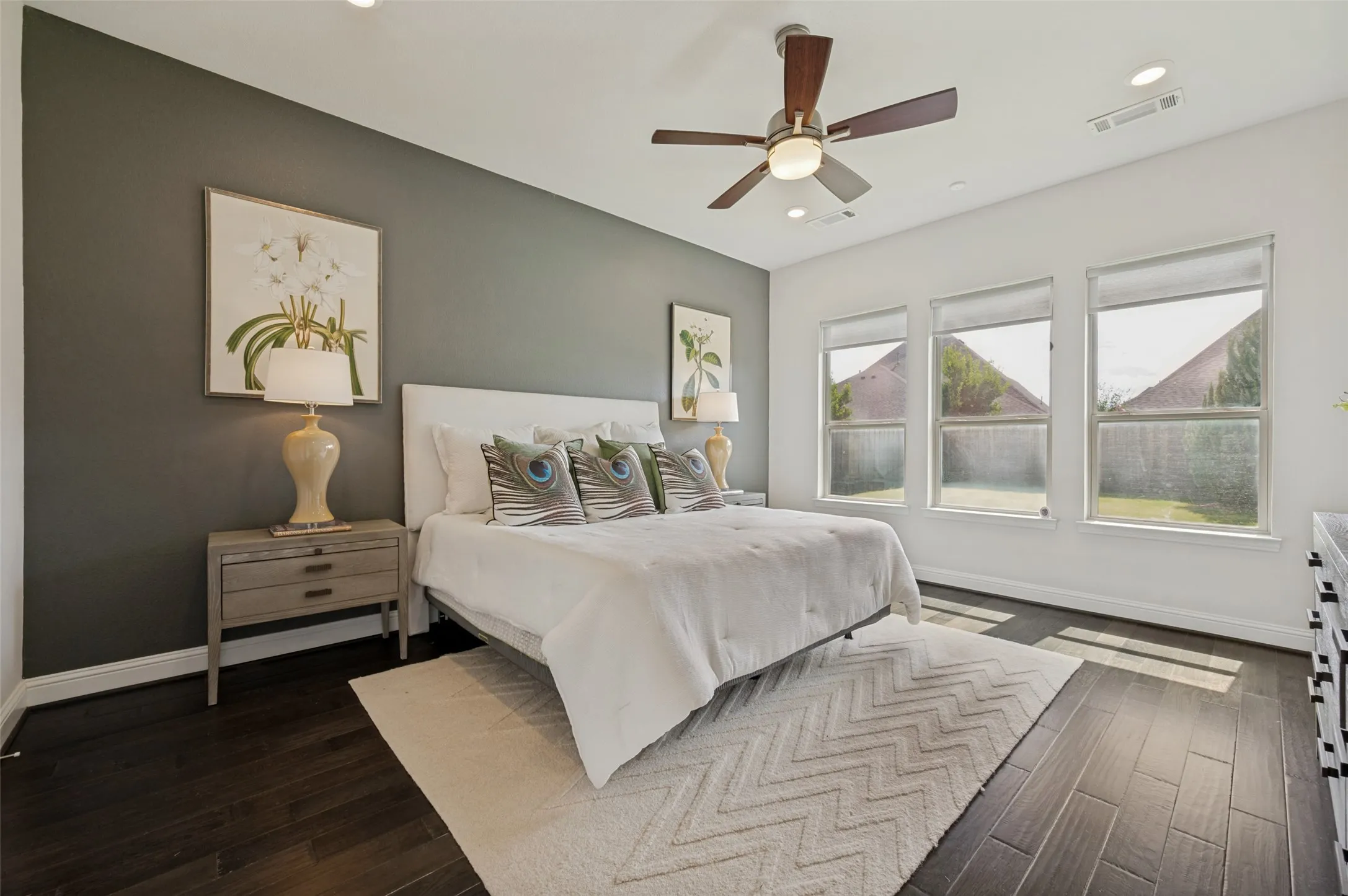 Private primary suite featuring wood floors, designer accent wall, and large windows overlooking the backyard.