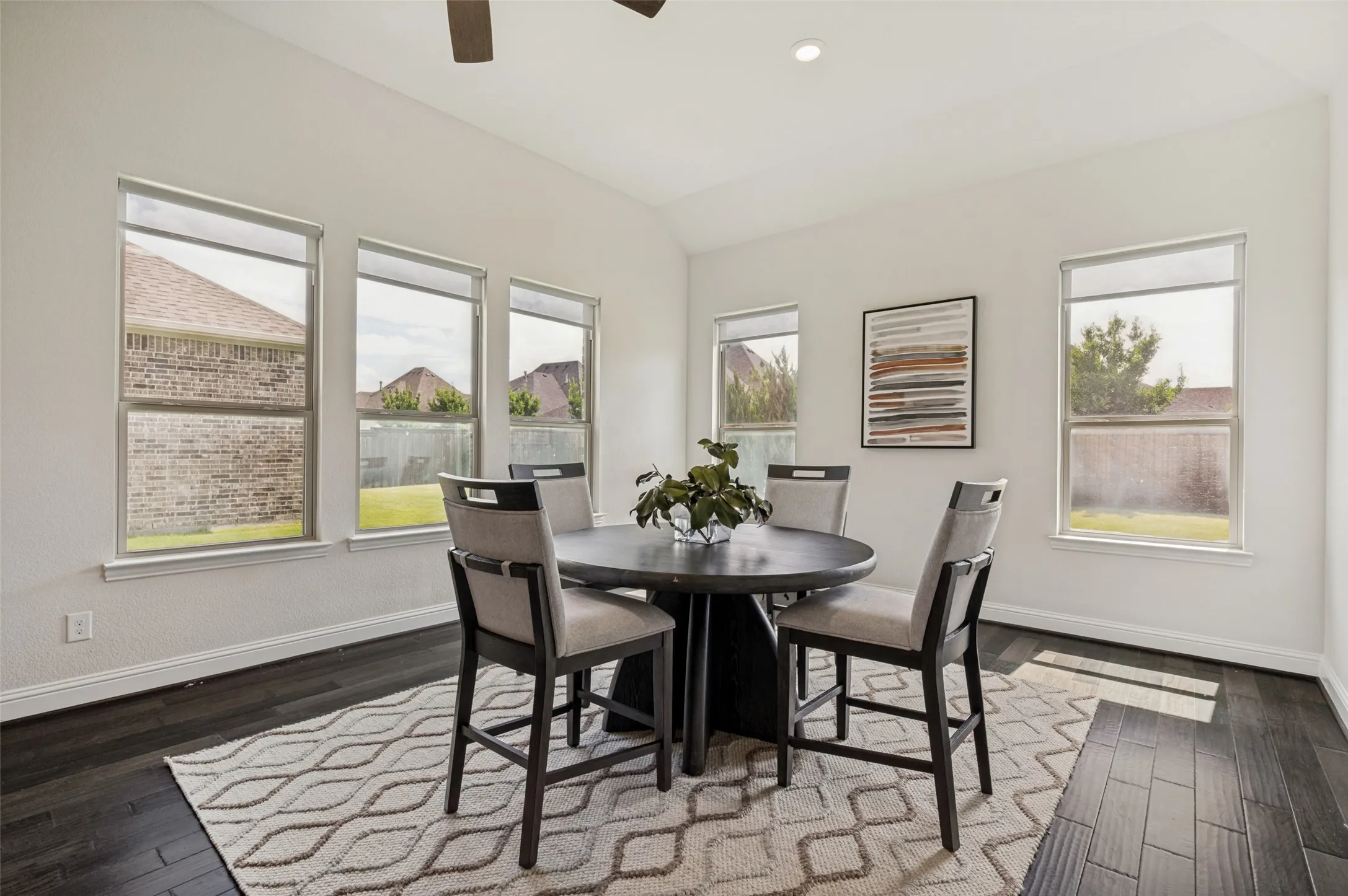 Spacious dining area filled with natural light and surrounded by windows overlooking the backyard.