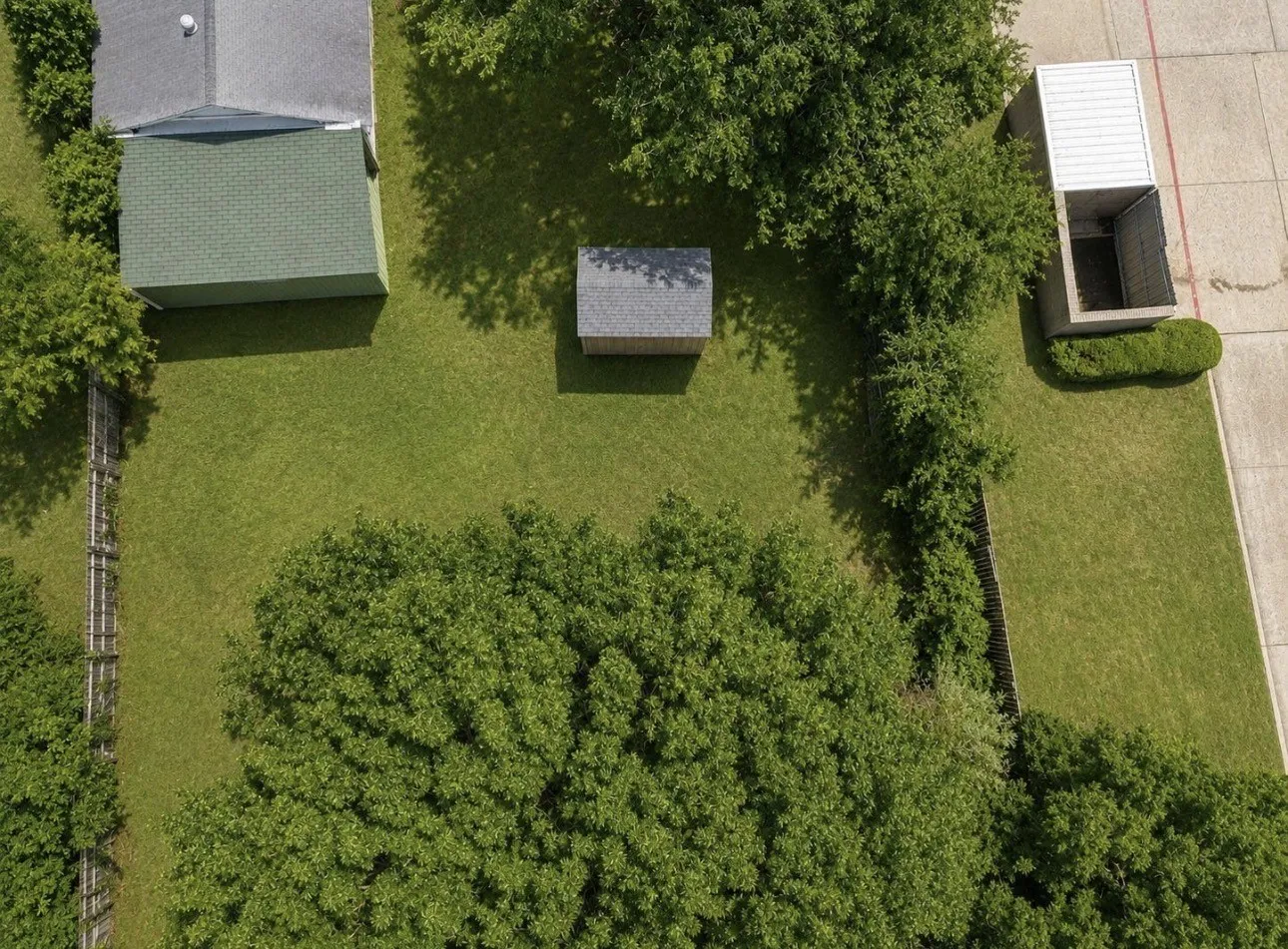 Expansive green lawn featuring a detached shed, established trees, and perimeter fencing