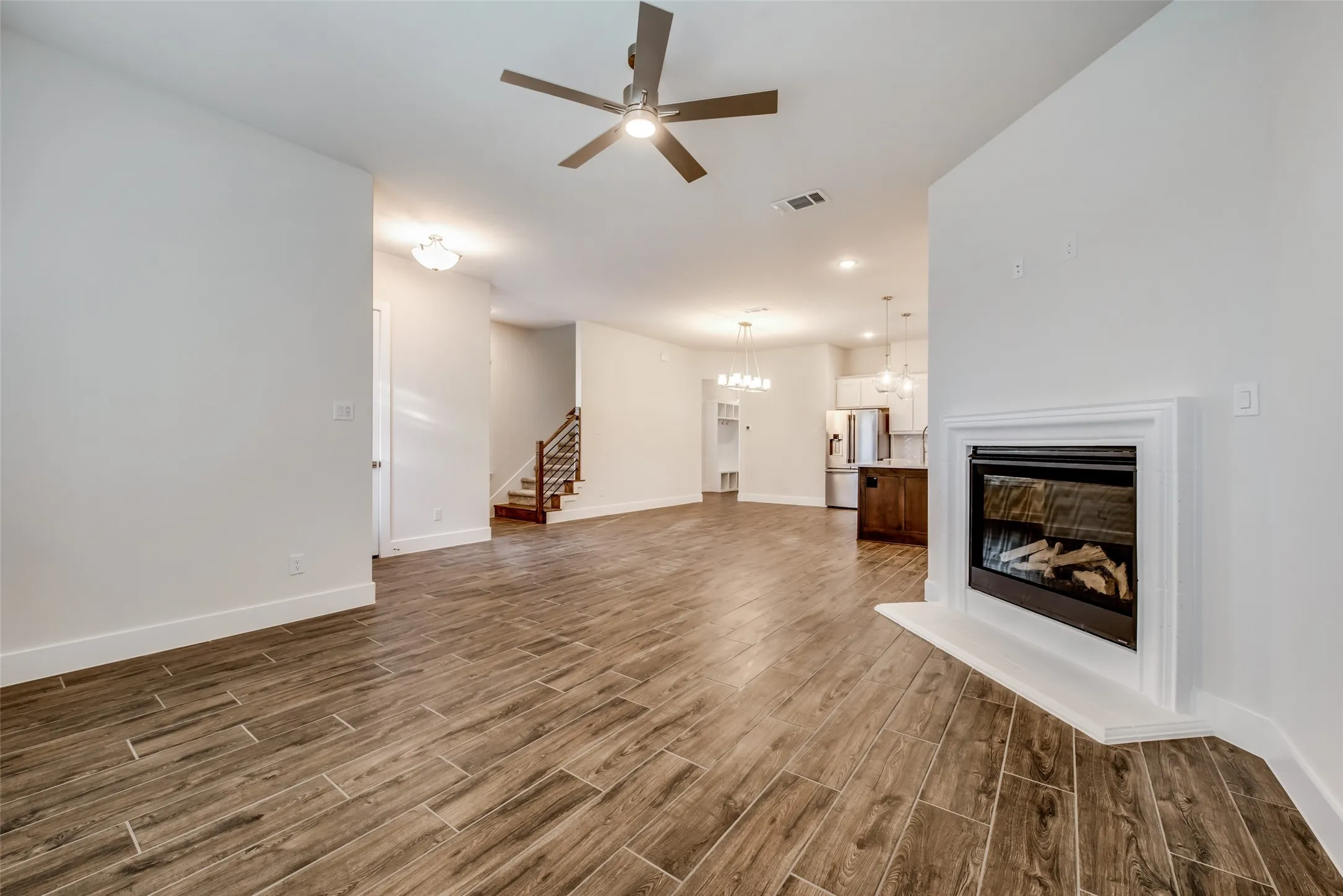 Spacious living area featuring wood-finish tile flooring, a contemporary ceiling fan, and a built-in fireplace with a white mantel