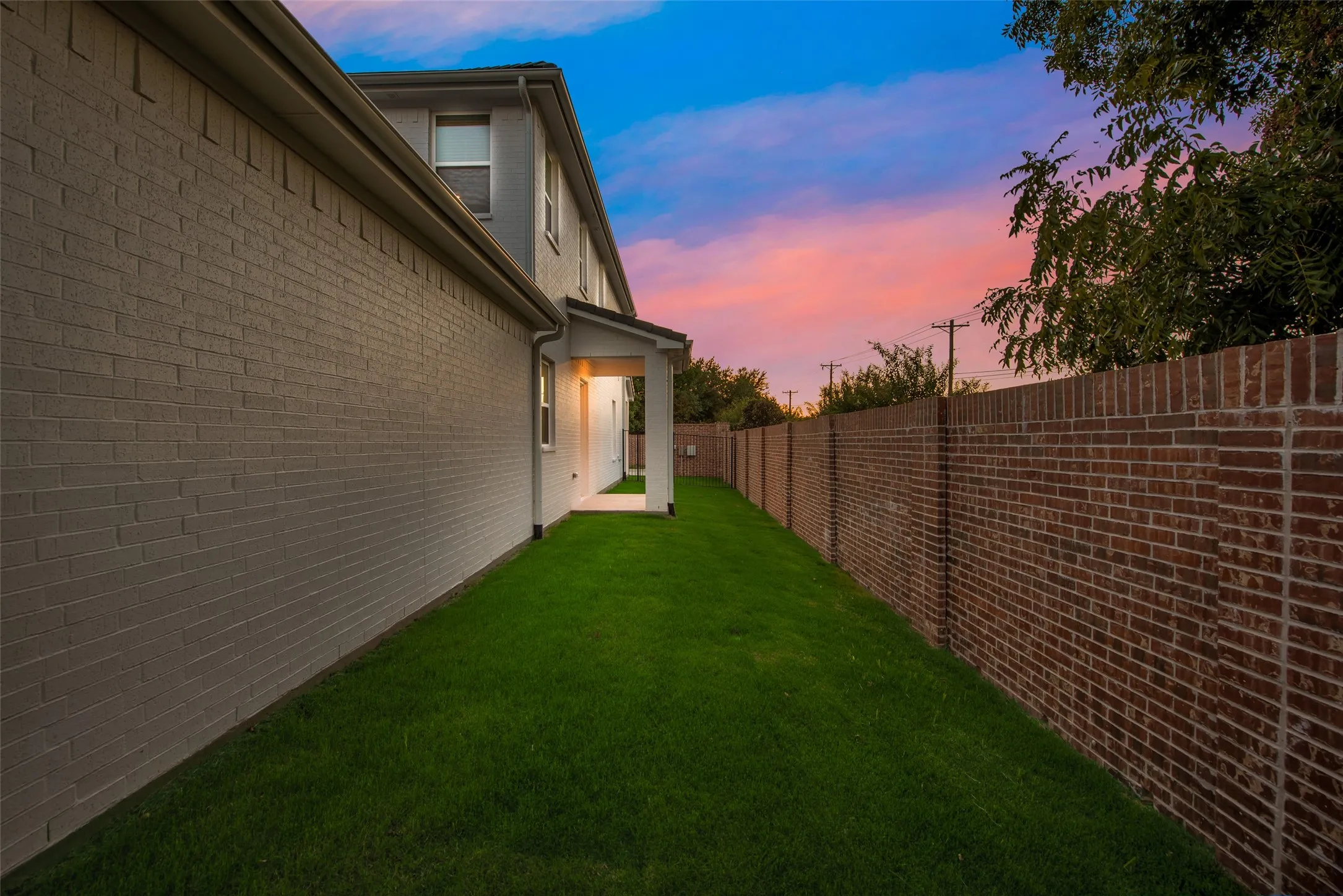 Side yard featuring a manicured lawn, painted brick exterior, and a privacy brick fence