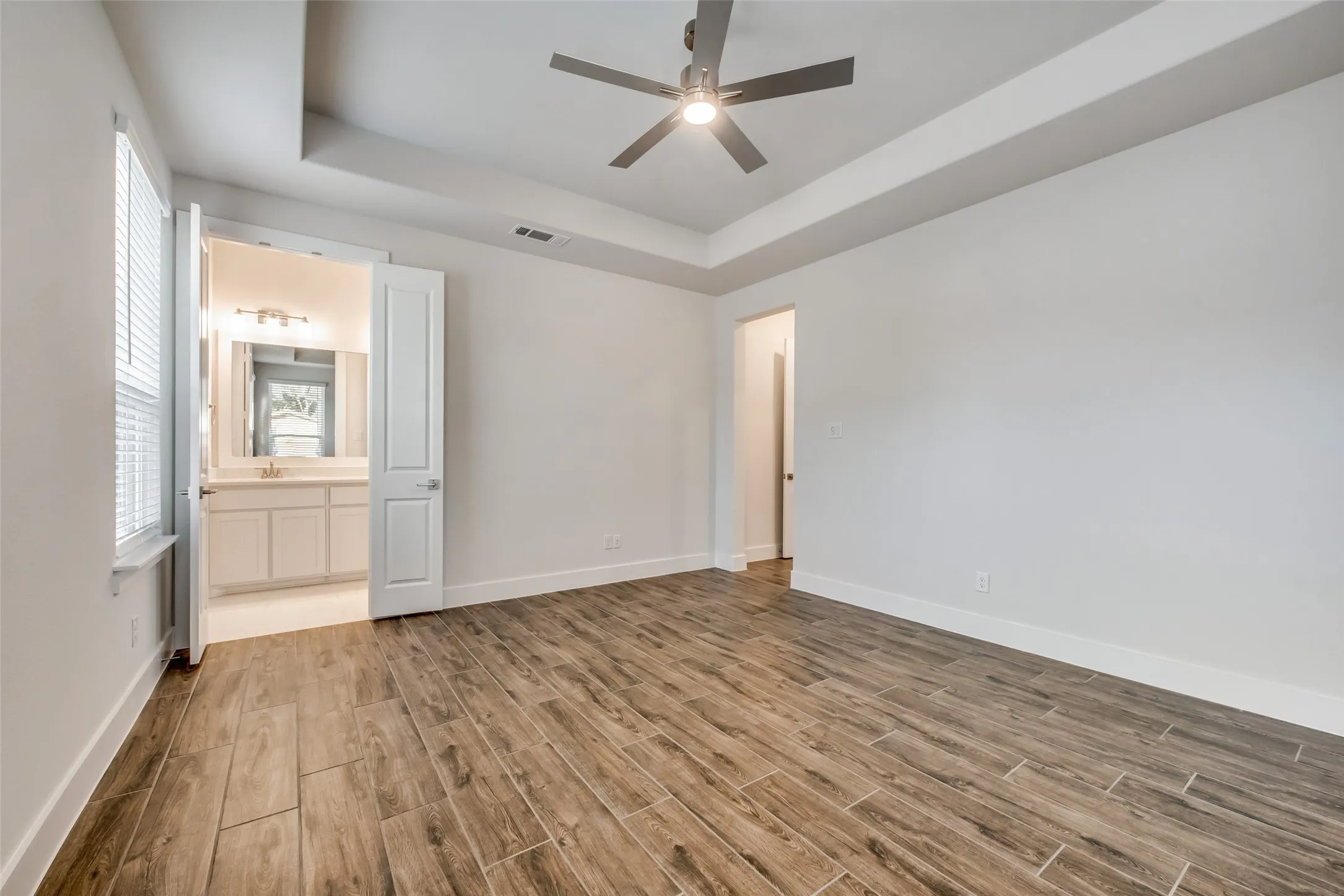 Spacious room featuring wood-finish flooring, a tray ceiling, and a ceiling fan