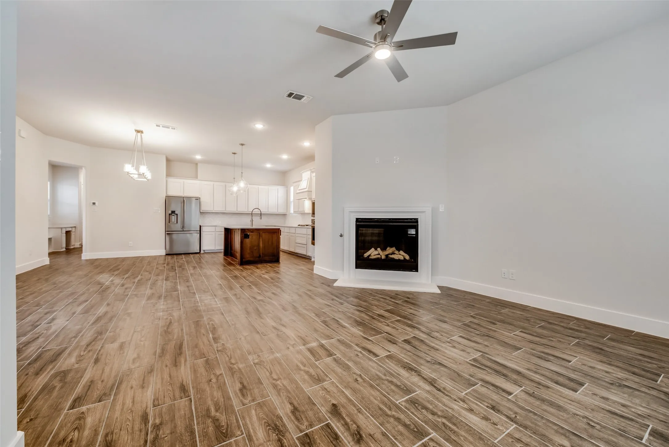 Expansive open-concept living area featuring wood-finish tile flooring, a built-in fireplace with a white mantel, and a ceiling fan