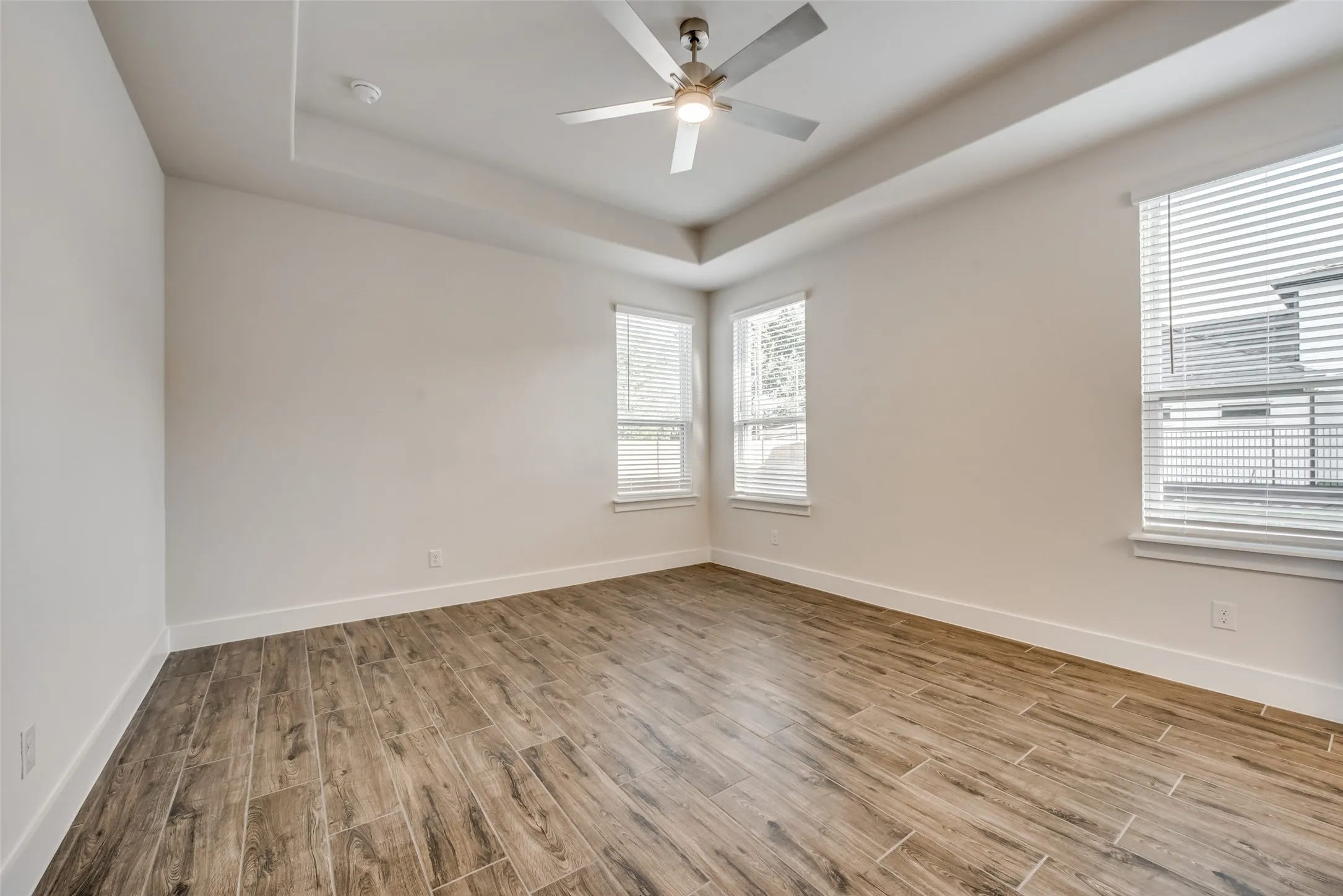 Spacious room featuring tray ceilings, wood-finish flooring, and white baseboards