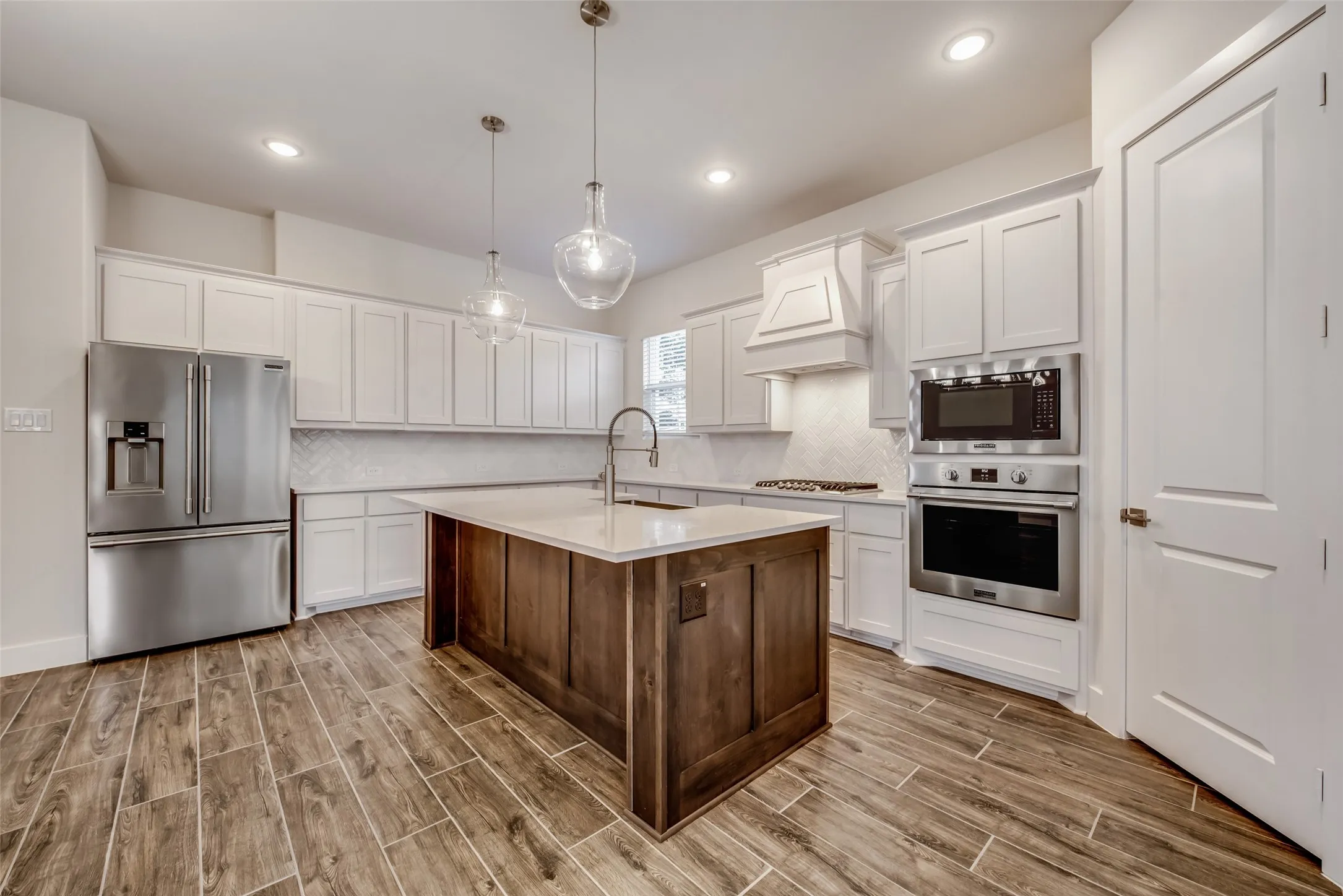 Modern kitchen featuring a wood-finish island with a countertop sink, stainless steel appliances, white cabinetry, and herringbone tile backsplash
