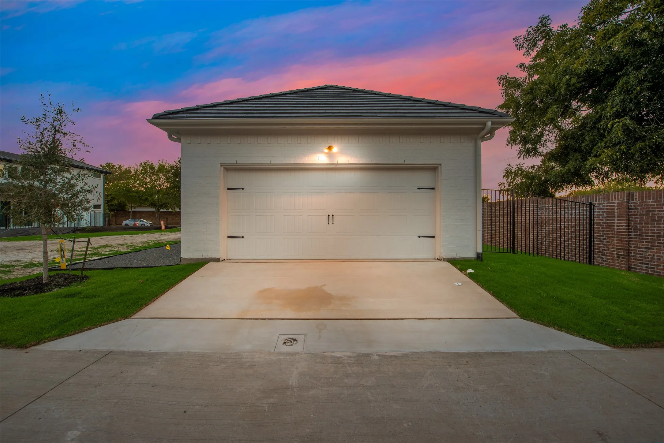 Detached garage featuring a white paneled door with decorative black hardware, white brick exterior, dark tile roof, and concrete driveway