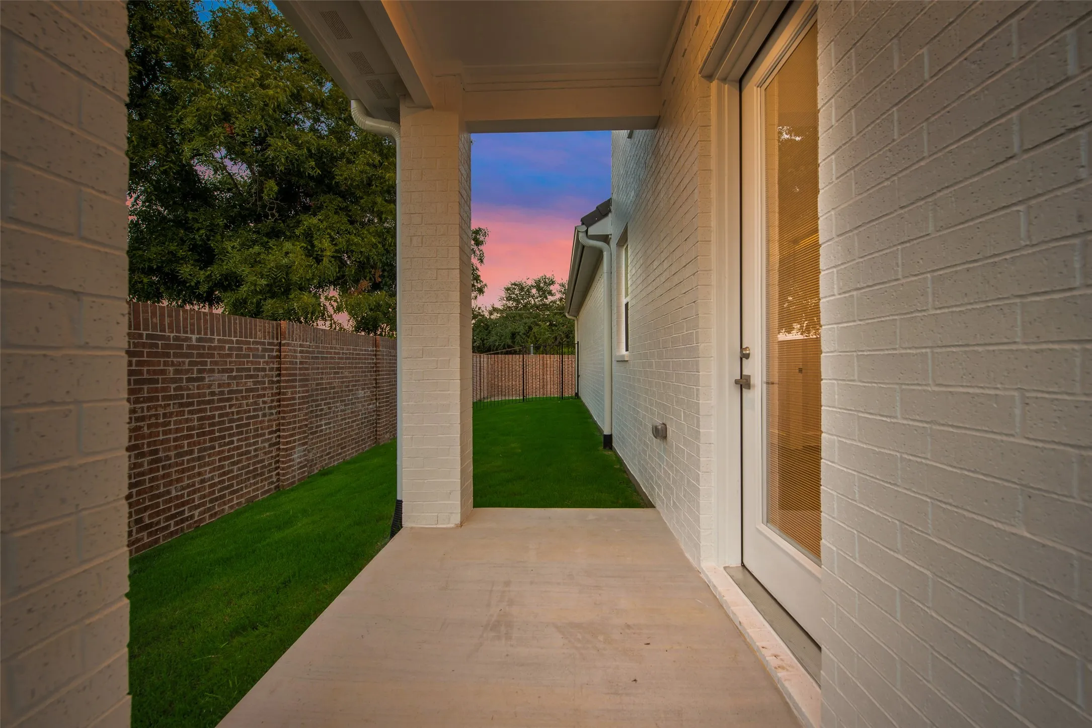 Covered patio with a concrete surface, white brick exterior, full-light glass door, and a manicured lawn