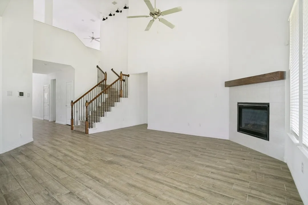 Two-story living area with high ceilings, wood-finish flooring, and a fireplace featuring a tile surround and wood mantel