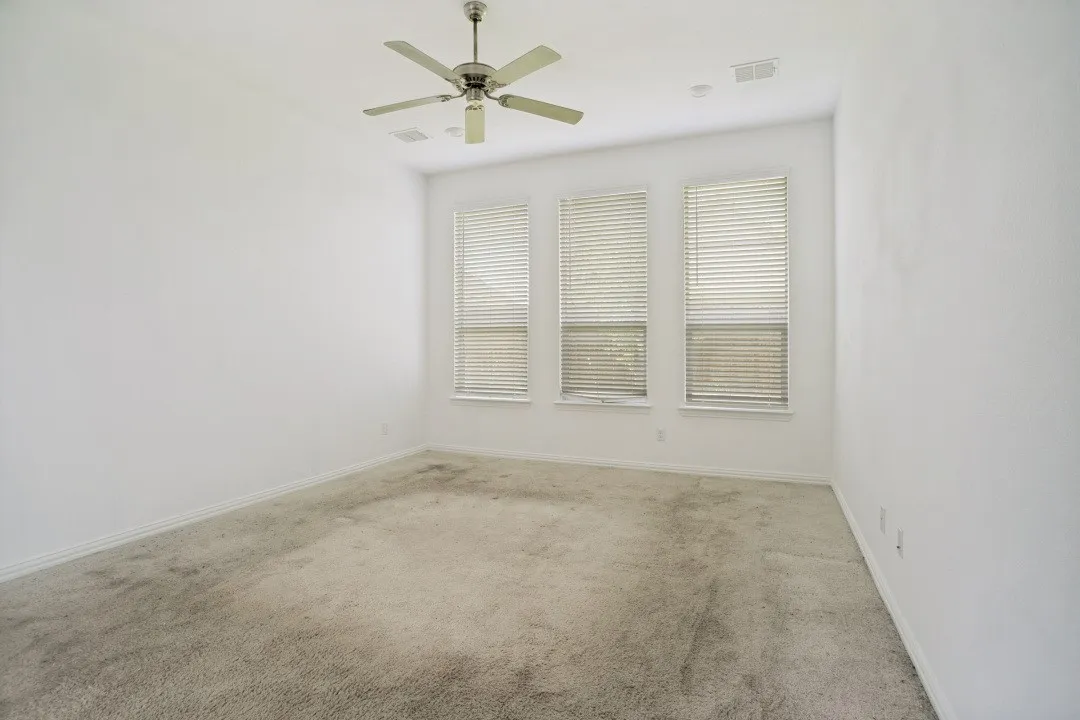 Room featuring three vertical windows with blinds, a ceiling fan, and light-colored carpet flooring