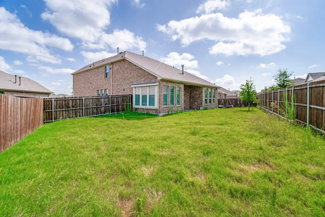 Expansive backyard featuring a manicured lawn, full privacy fencing, and a brick-sided exterior with multiple windows