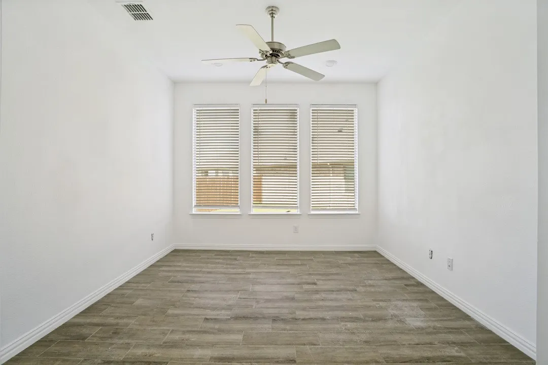 Room featuring three windows with blinds, a ceiling fan, white baseboards, and wood-finish flooring