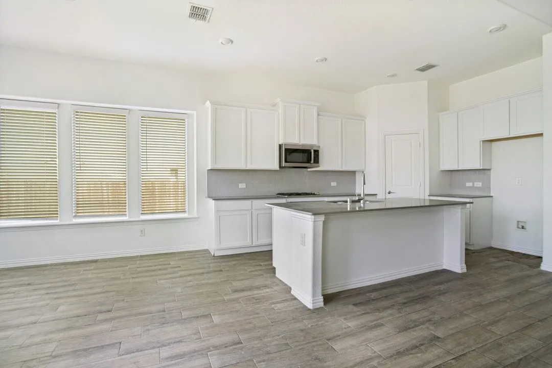 Open-concept kitchen featuring an island, white cabinetry, stainless steel microwave, gray tile backsplash, and wood-finish flooring